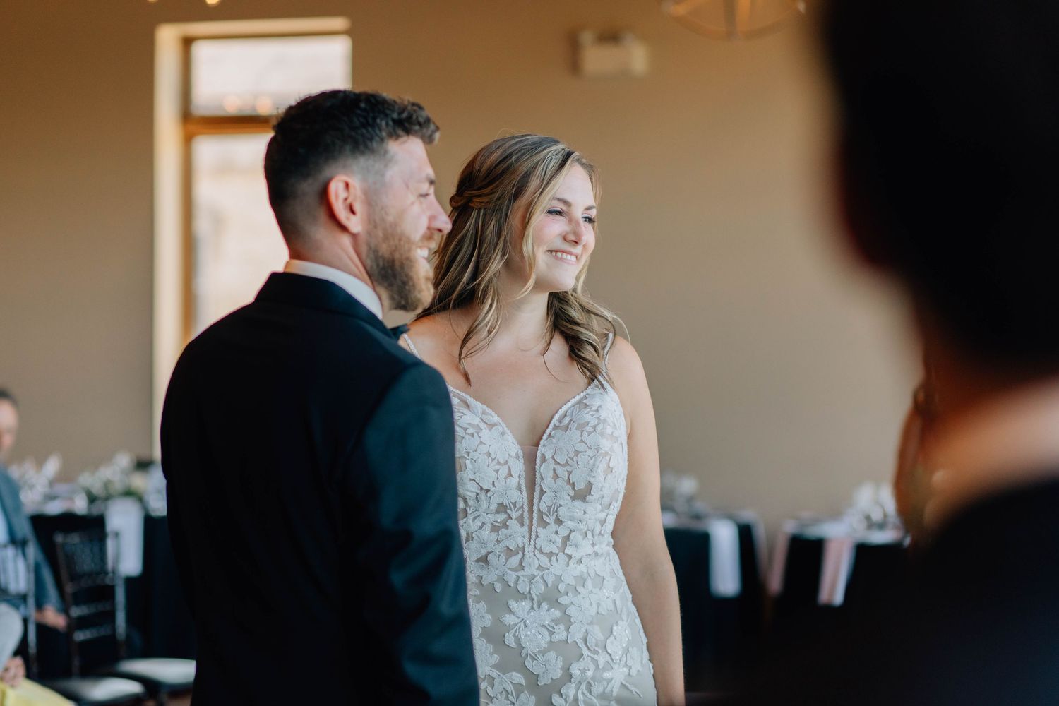 Bride smiling joyfully at groom during indoor wedding ceremony in elegant venue.