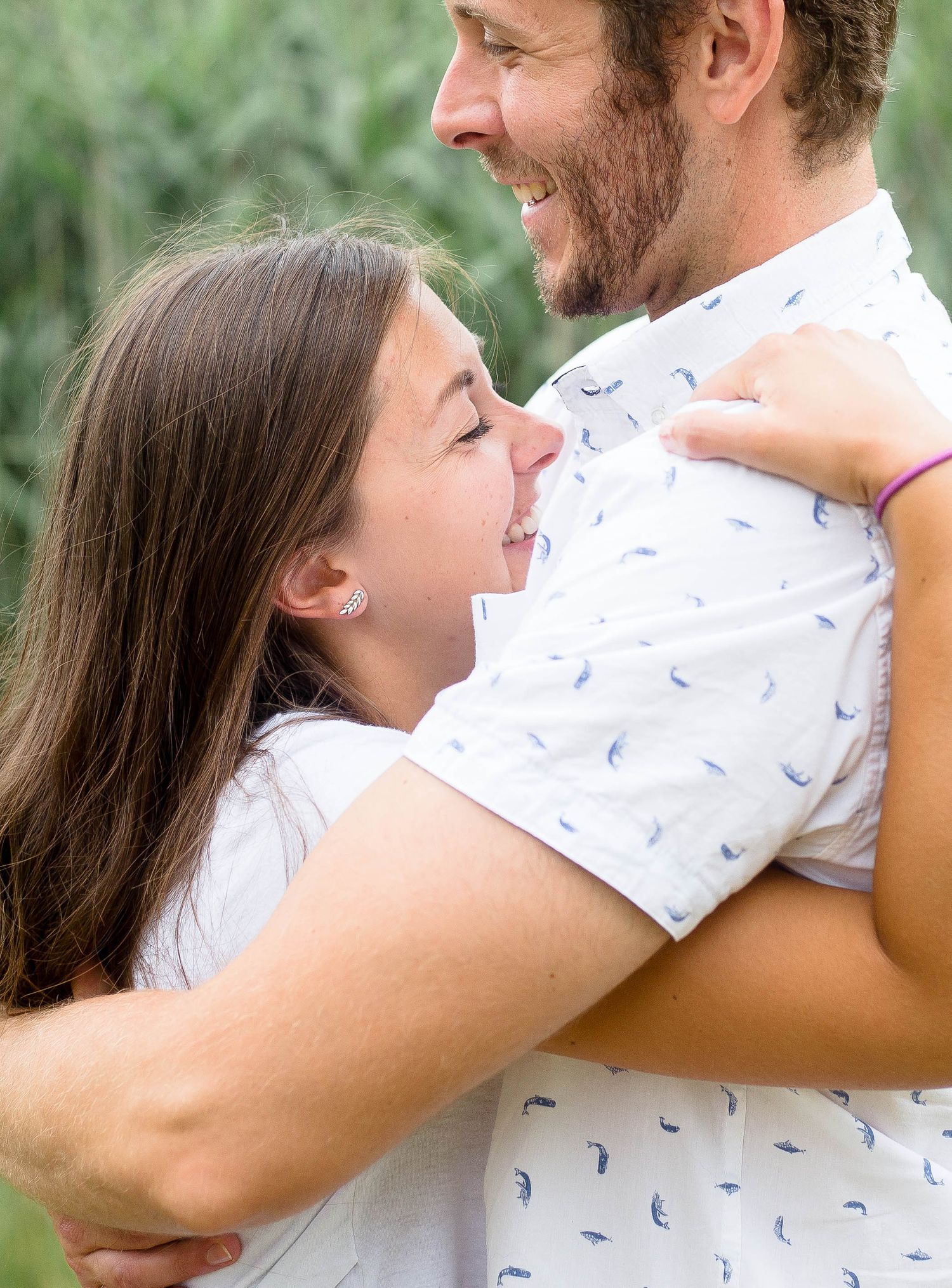 Woman hugging man and laughing joyfully in an outdoor green setting.
