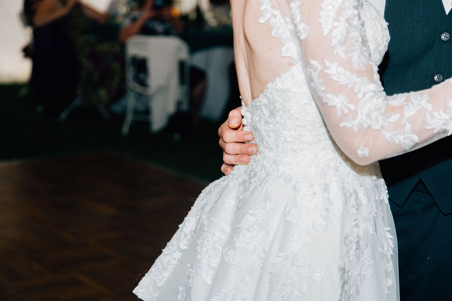 Close-up of groom holding bride in beautiful lace wedding dress during their first dance.