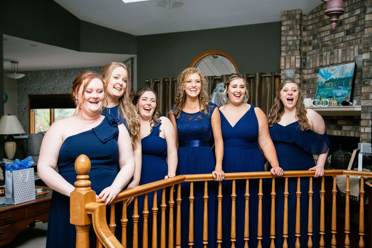 Five bridesmaids in navy blue dresses laughing and posing together at a wooden staircase railing before wedding.