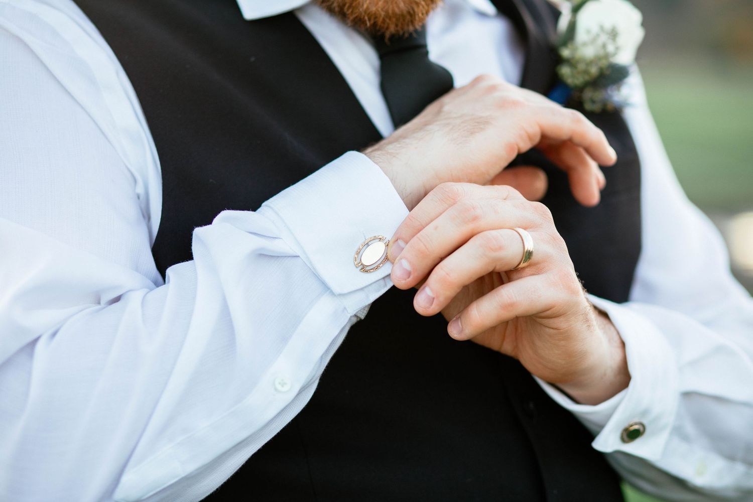 Close-up of groom adjusting his cufflinks wearing a white dress shirt and black vest.