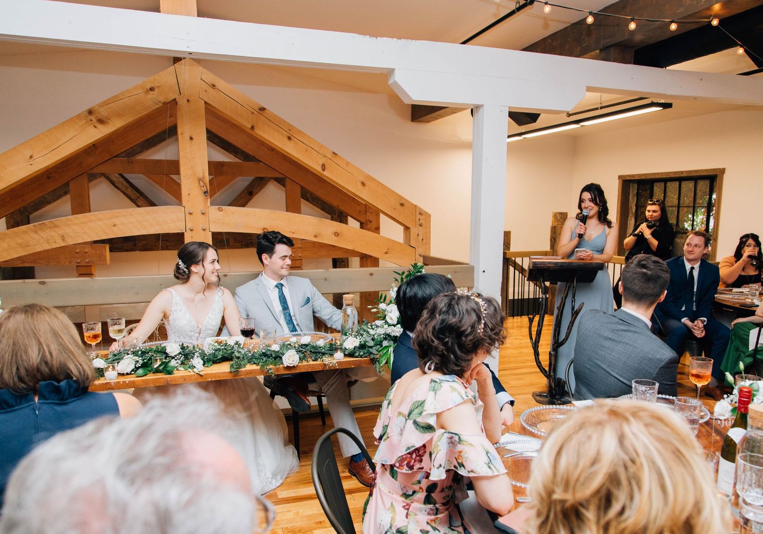Bride and groom seated at sweetheart table during elegant rustic barn wedding reception.