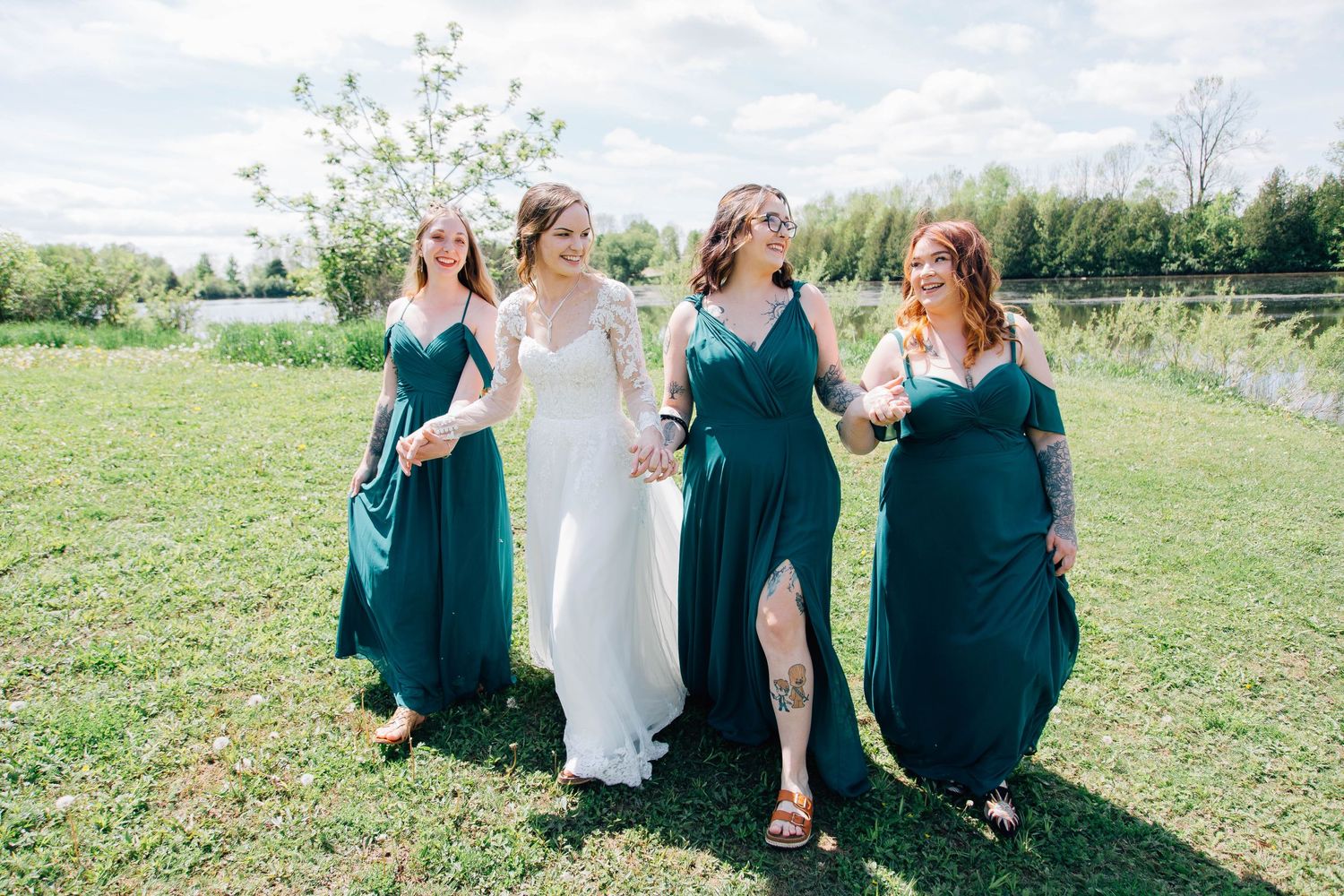 Bride and bridesmaids in emerald green gowns walking hand in hand on green lawn.