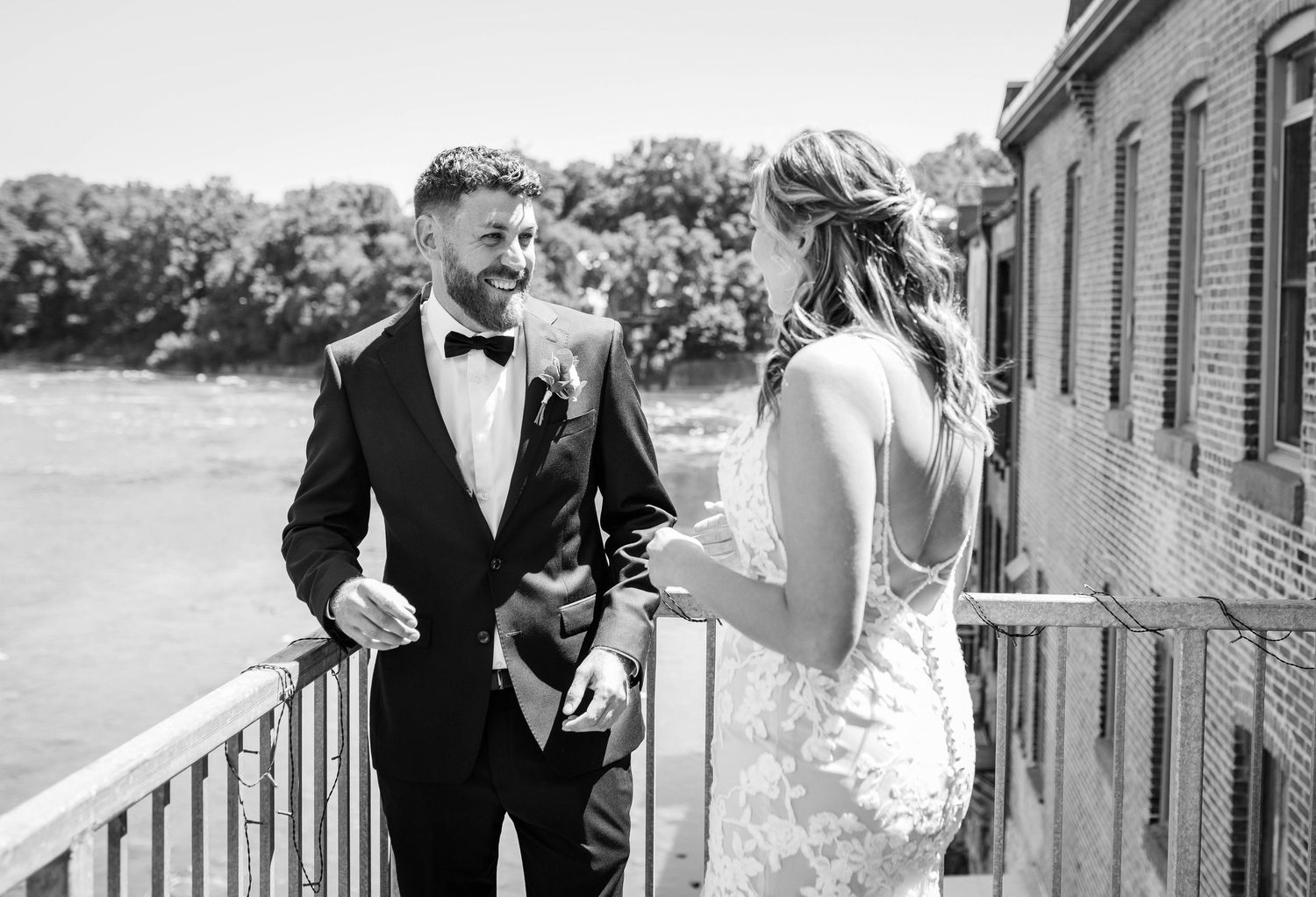 Groom smiling at bride during outdoor first look on balcony in black and white photo.