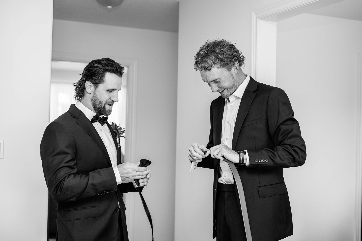 Two men in tuxedos checking details before wedding in black and white photo.