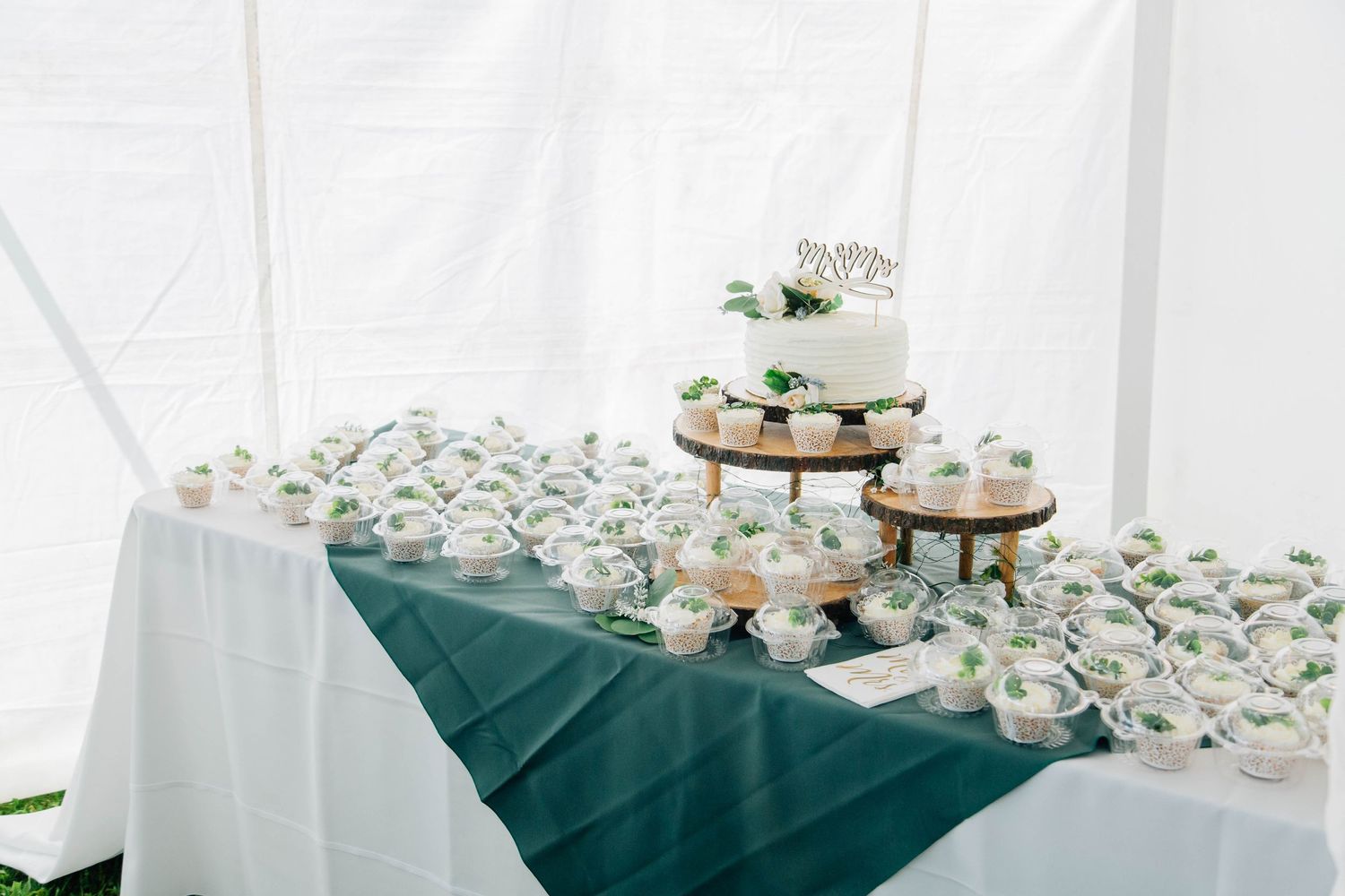 Wedding dessert table featuring a tiered cake and cupcakes with green leaf decorations.