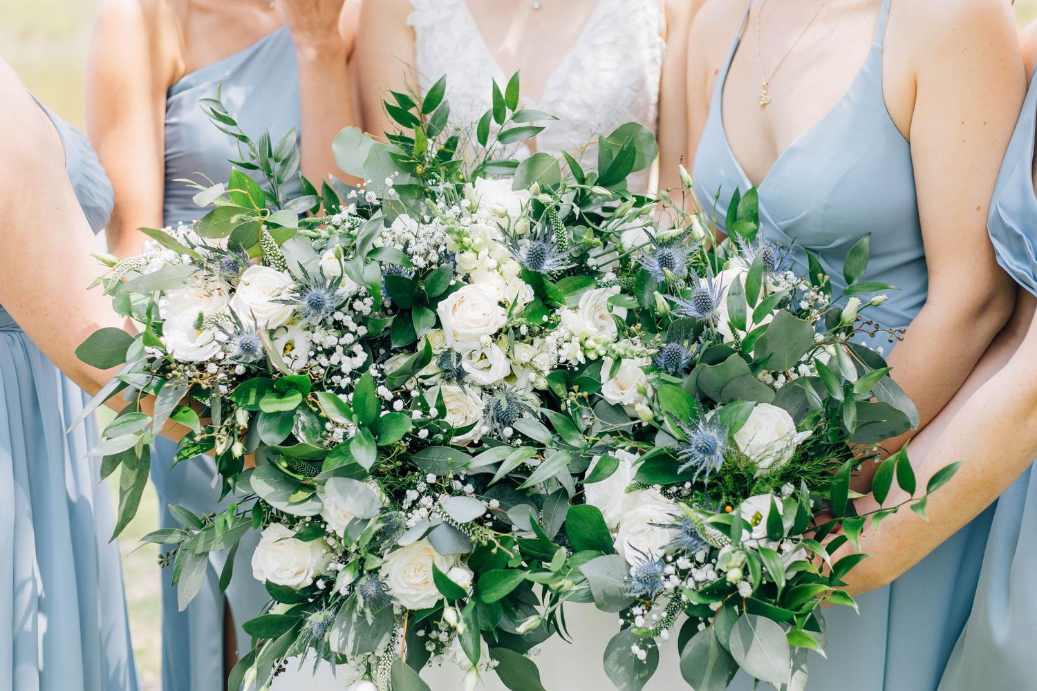 Close-up of wedding bouquets featuring white roses, thistle, and eucalyptus held by bridesmaids in blue.