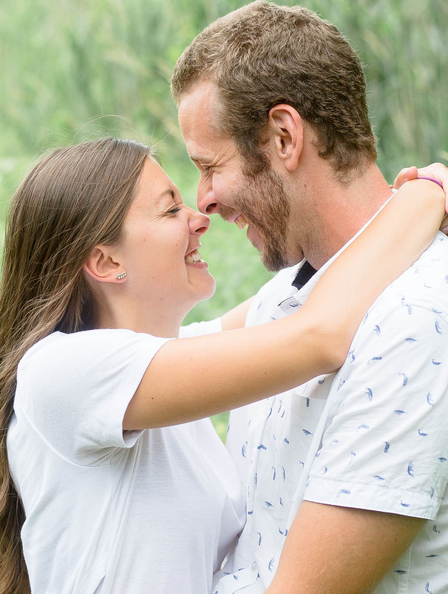 A laughing couple gazes into each others eyes during a joyful outdoor engagement photo session.