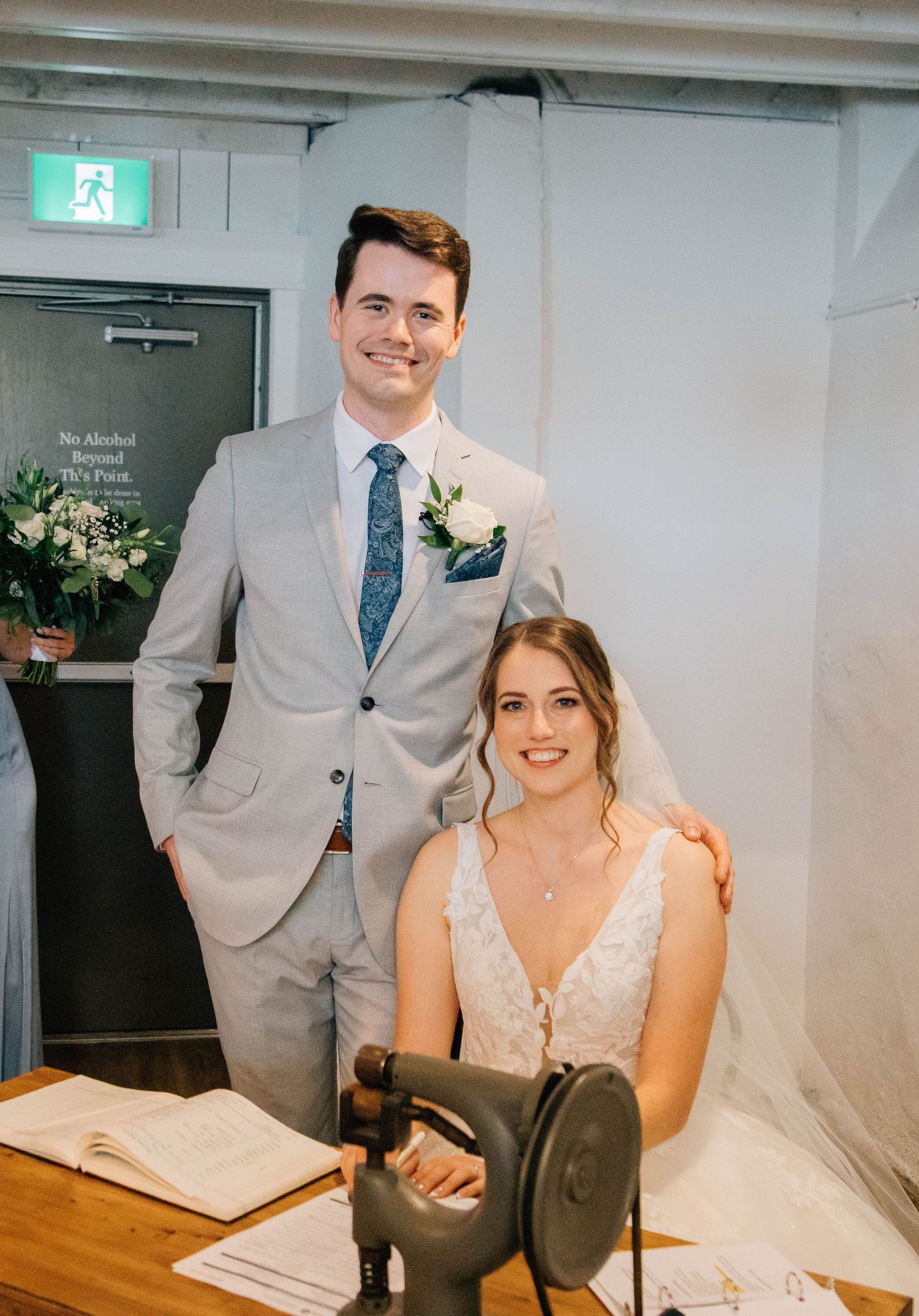 Smiling bride and groom posing together while signing wedding registry documents.