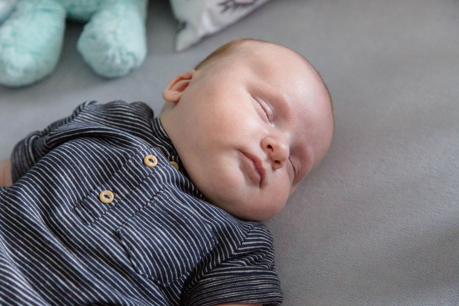 Peaceful newborn baby sleeping in gray striped onesie on soft light gray surface.