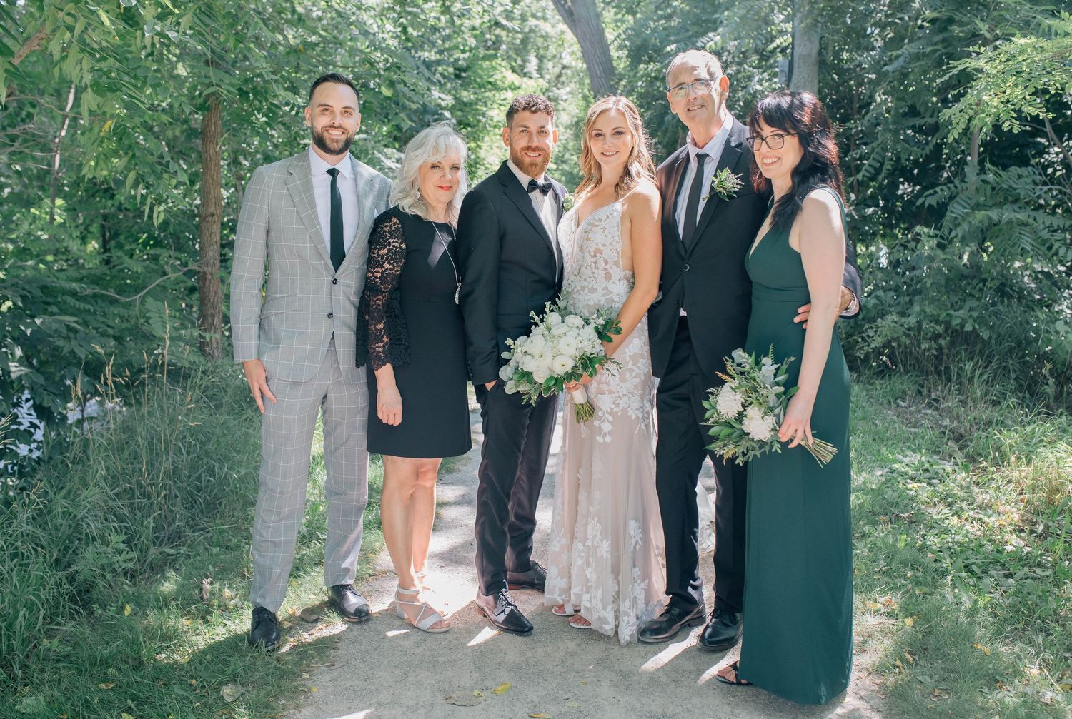 Bride's family posing together in a lush green outdoor setting with bride in lace gown.