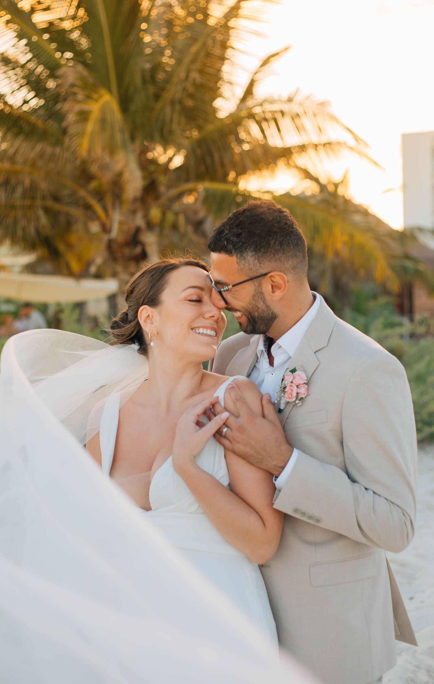 Bride and groom embracing on a tropical beach at sunset, smiling joyfully in wedding attire in Cancun Mexico.