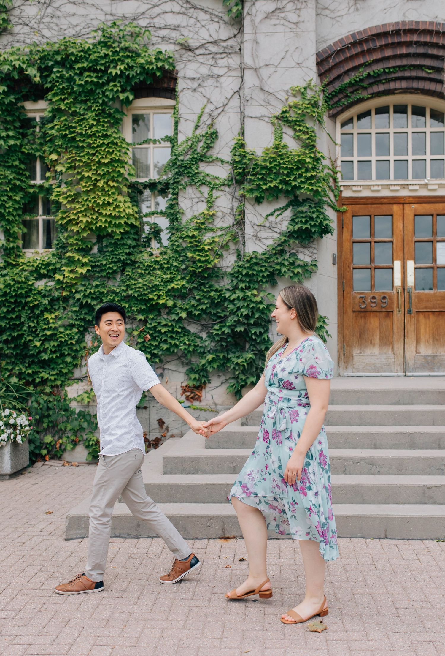 Happy couple holding hands and walking outside an ivy-covered stone building with wooden doors.