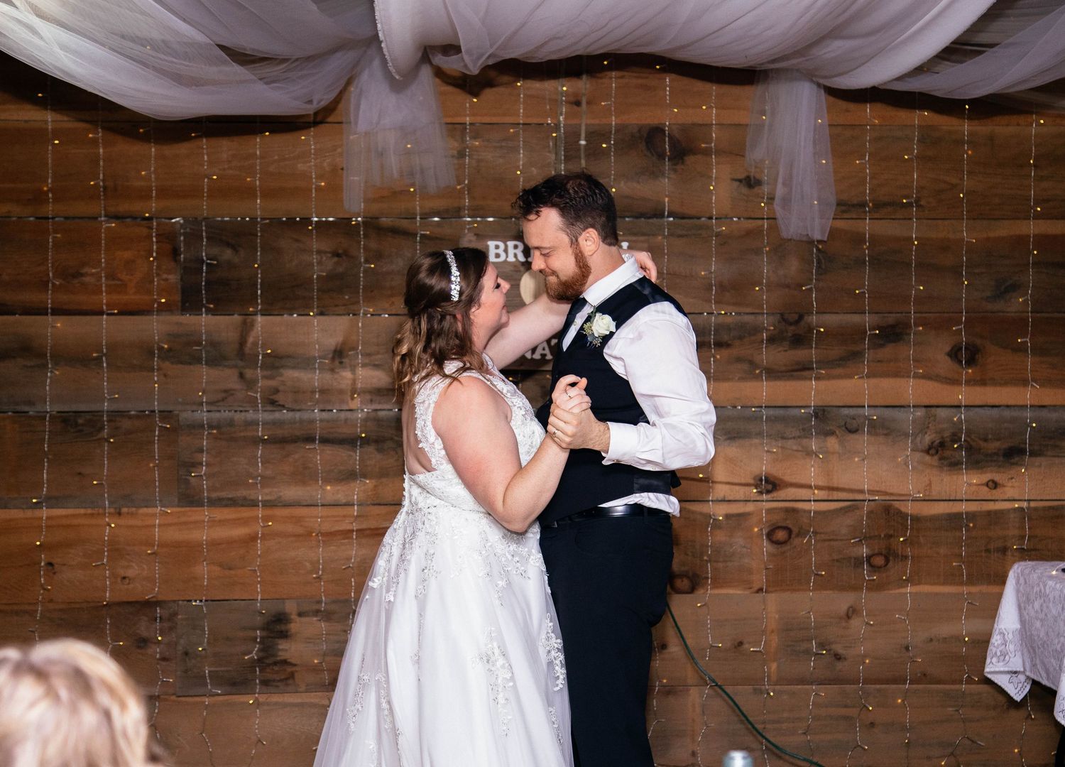 Bride and groom sharing their first dance at rustic barn wedding reception with string lights.
