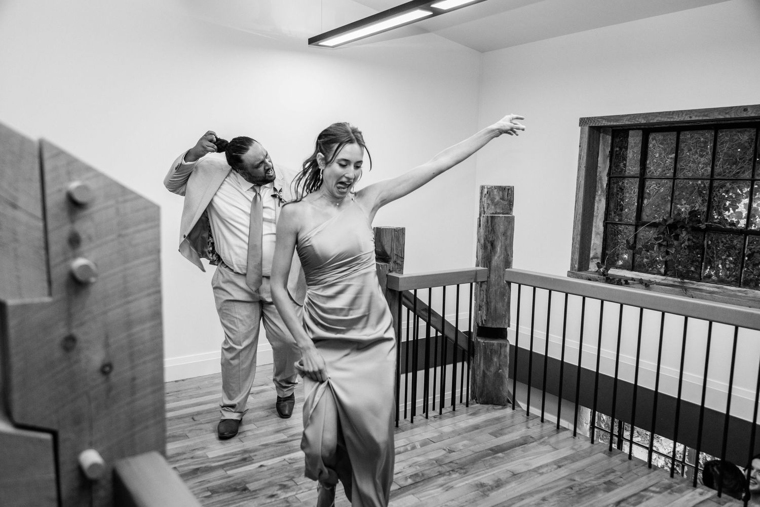 Black and white photo of bridesmaid and groomsman dancing together at wedding reception entrance.
