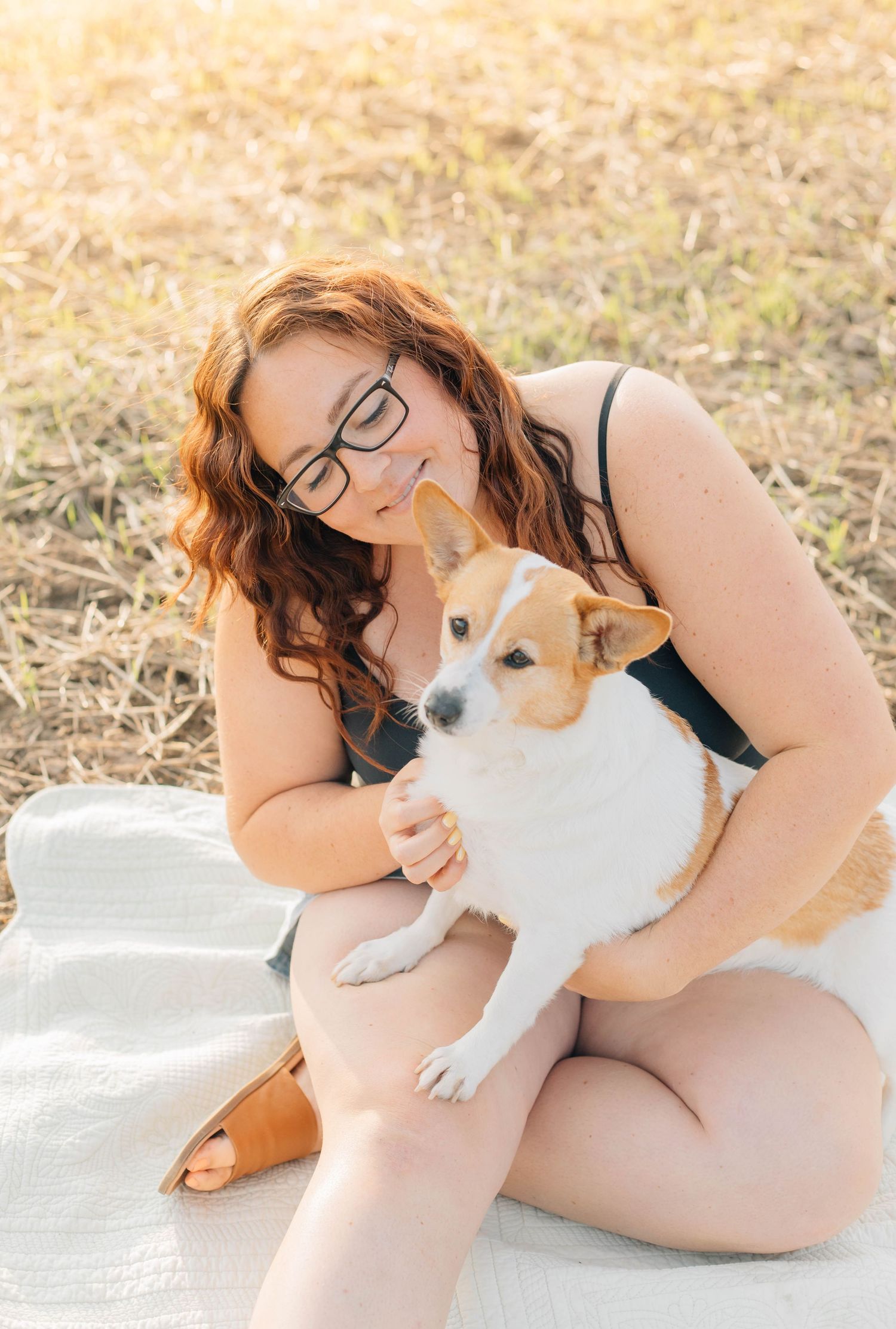 Woodstock wedding photographer cuddling corgi dog outdoors on blanket.