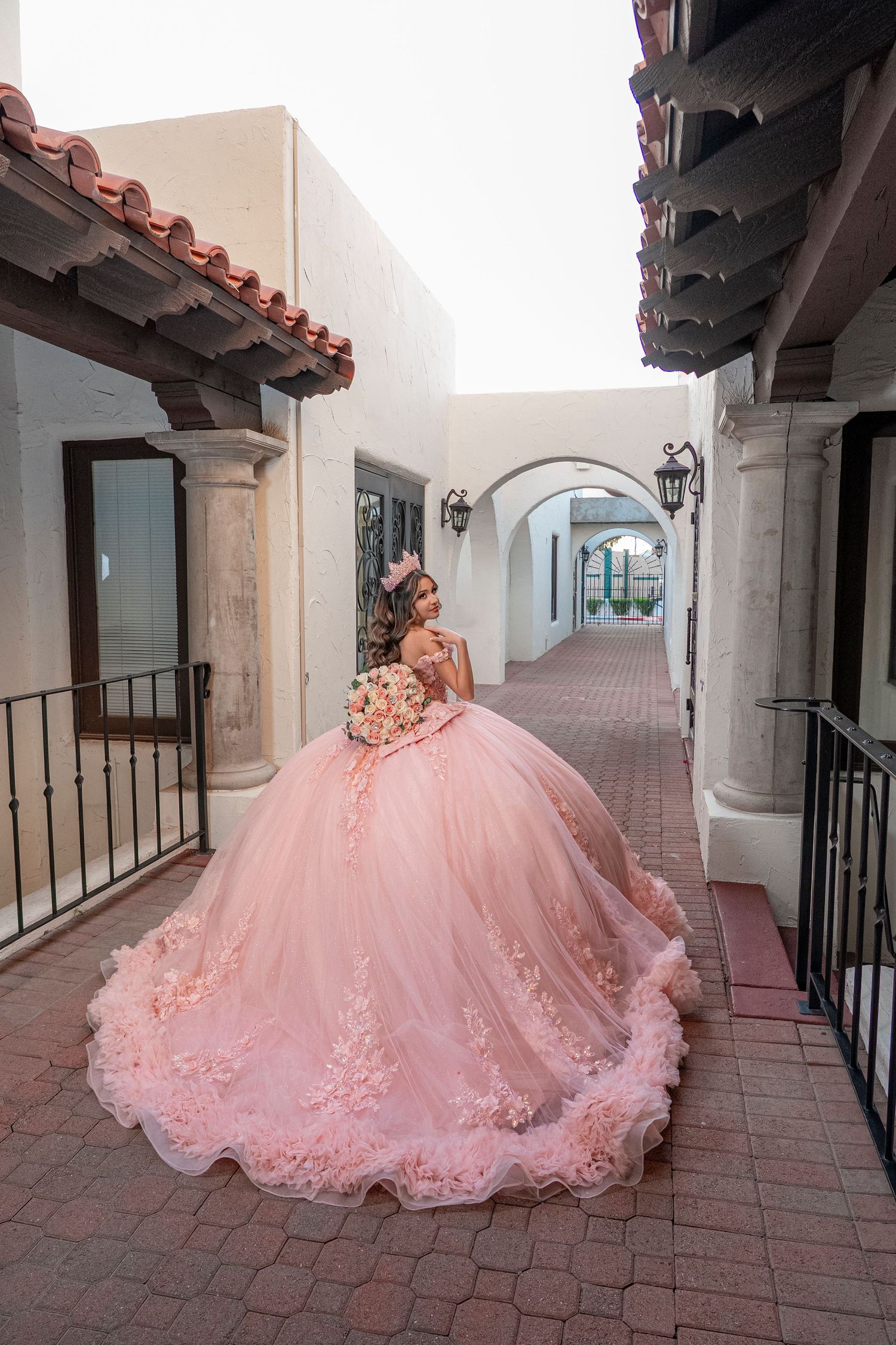 Young woman in a stunning pink ball gown quinceañera dress poses in an elegant Spanish-style courtyard.