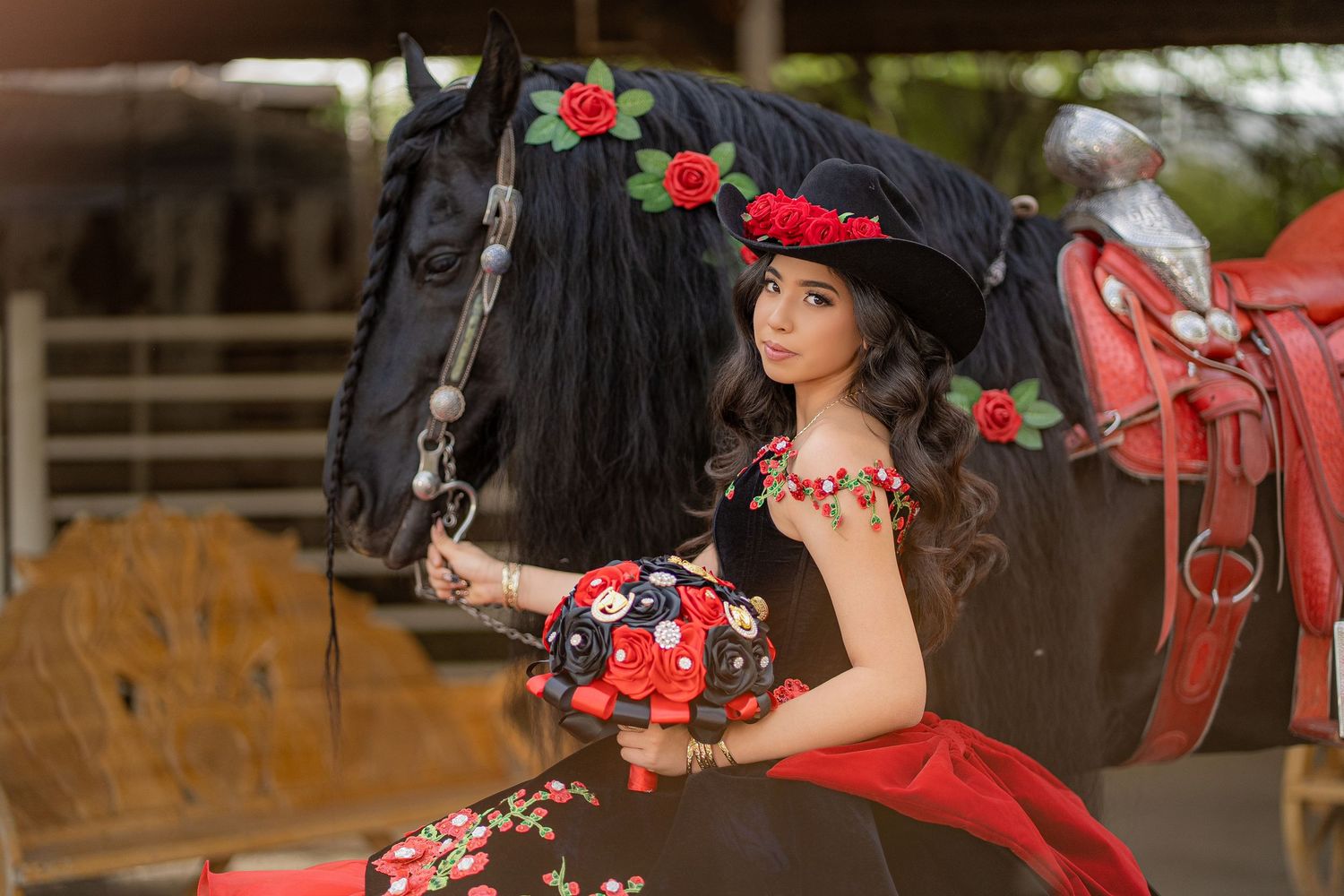Young woman in red floral dress and hat poses with a black horse decorated with red roses outdoors.