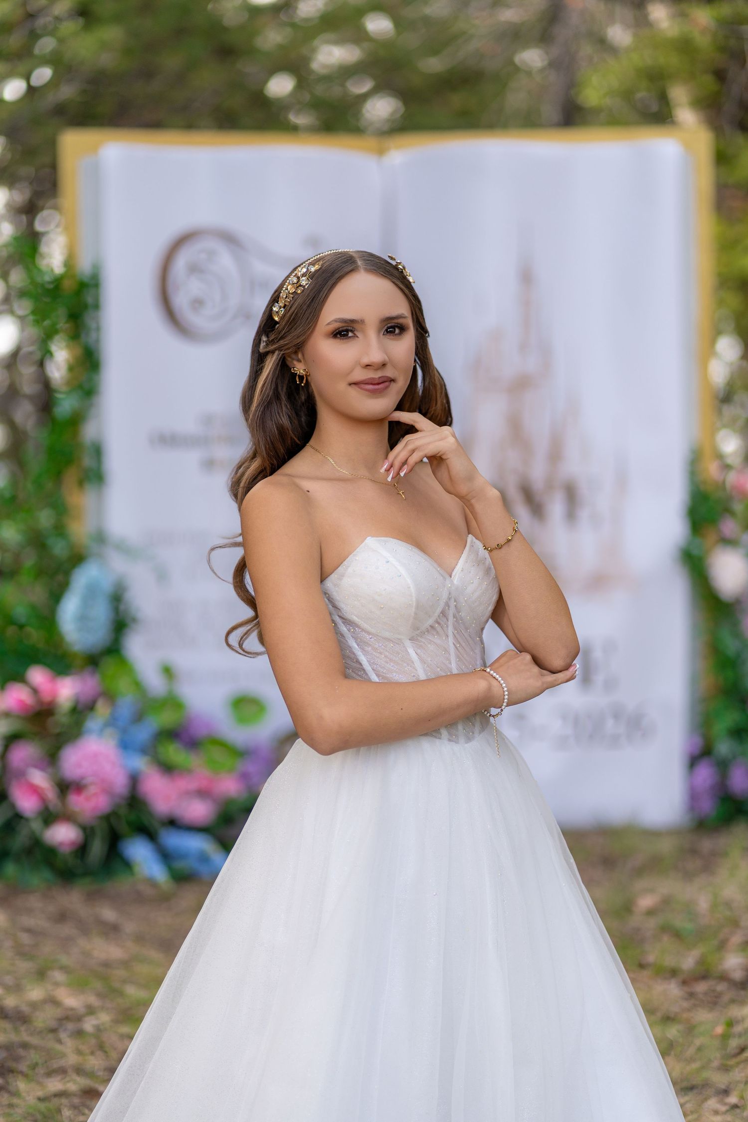 Elegant young woman in white strapless ball gown with gold hair accessory poses outdoors.