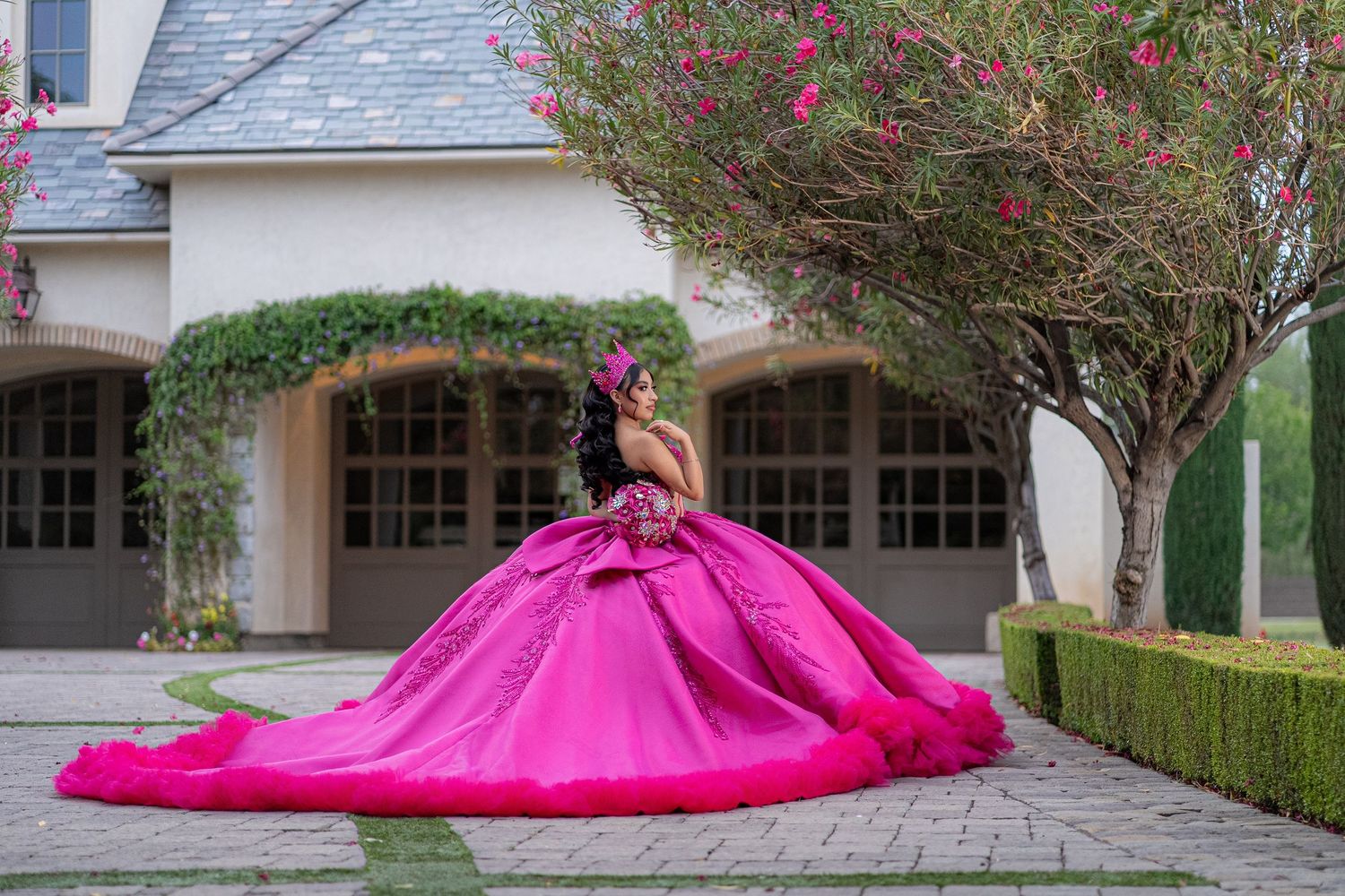 Young woman in a stunning hot pink ball gown quinceañera dress poses gracefully outdoors near a elegant building.
