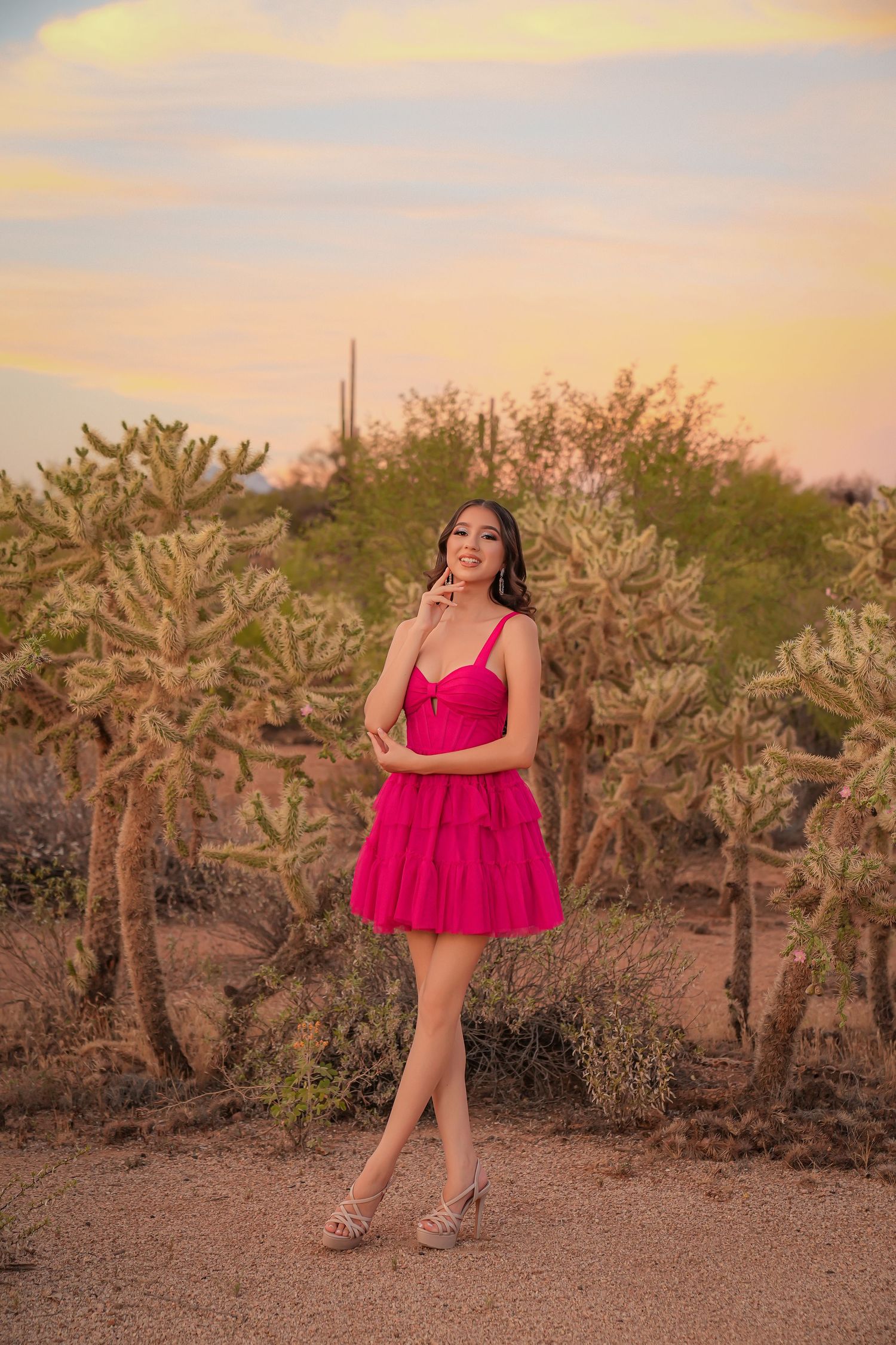 Young woman in pink mini dress posing among desert cacti at sunset in Arizona.