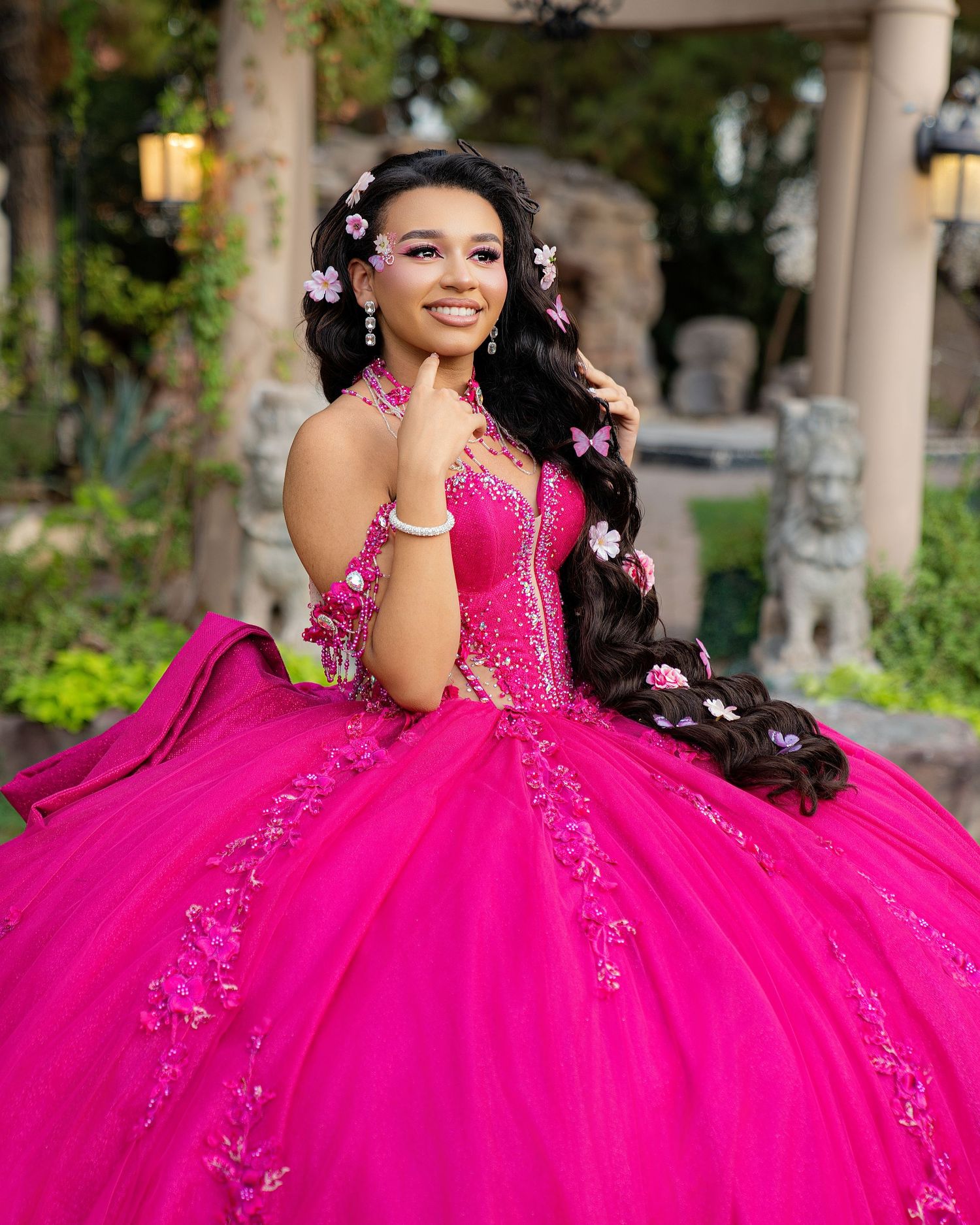 Young woman in a vibrant hot pink quinceañera ball gown with floral accents and flowers in her long dark hair.