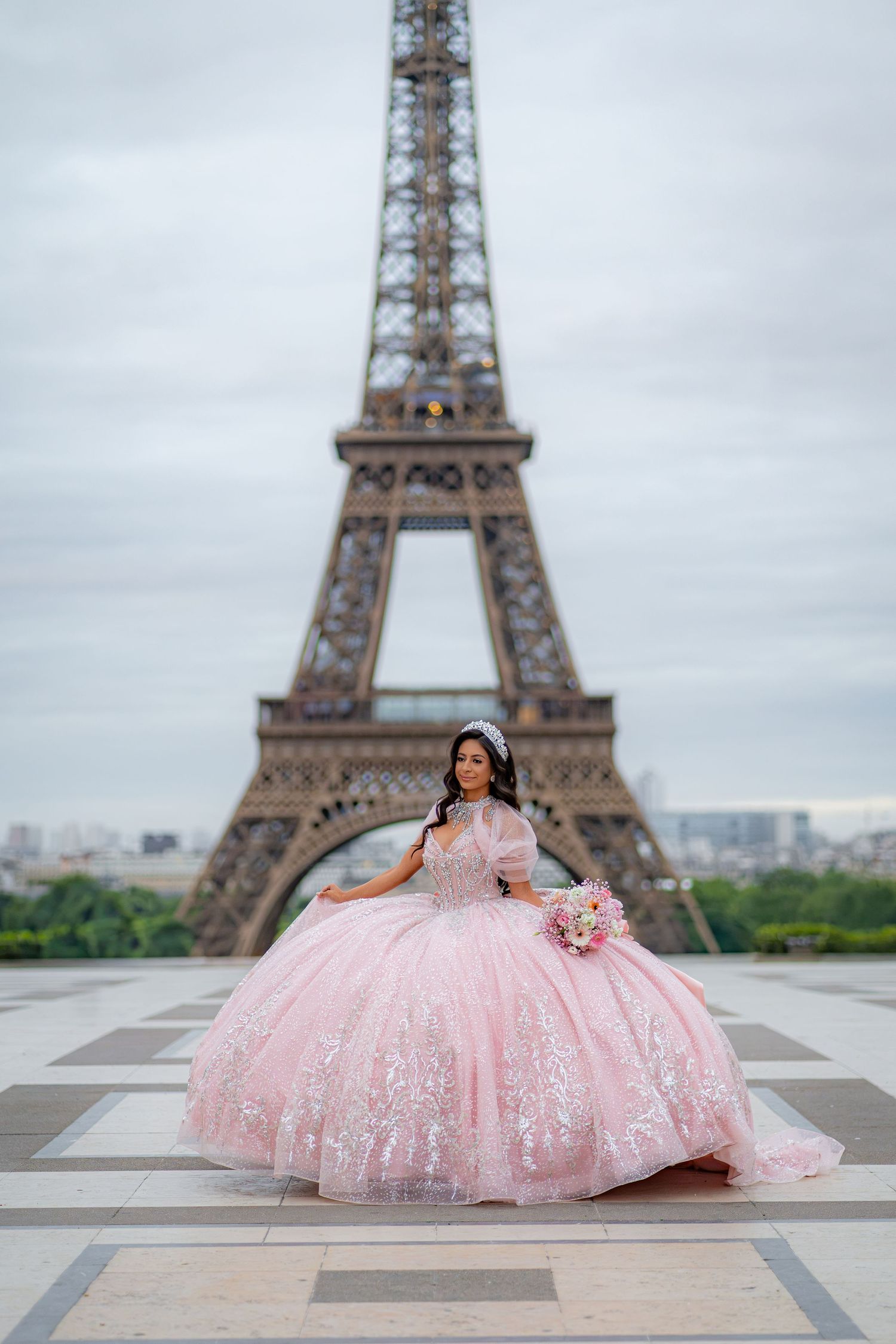 Young woman in pink quinceañera ball gown poses in front of the Eiffel Tower in Paris.