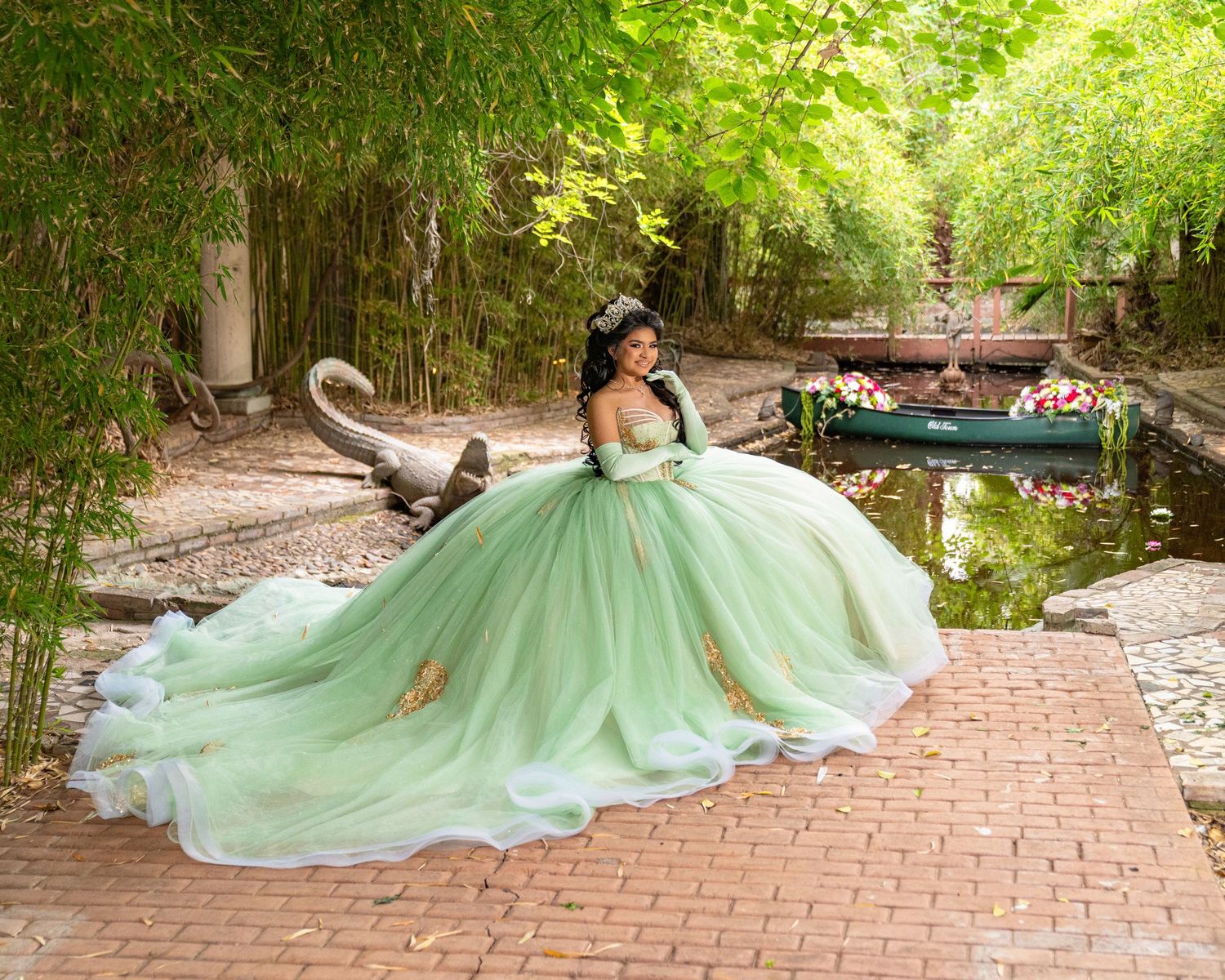 Young woman in a mint green quinceañera ball gown with gold accents poses near a serene garden pond.