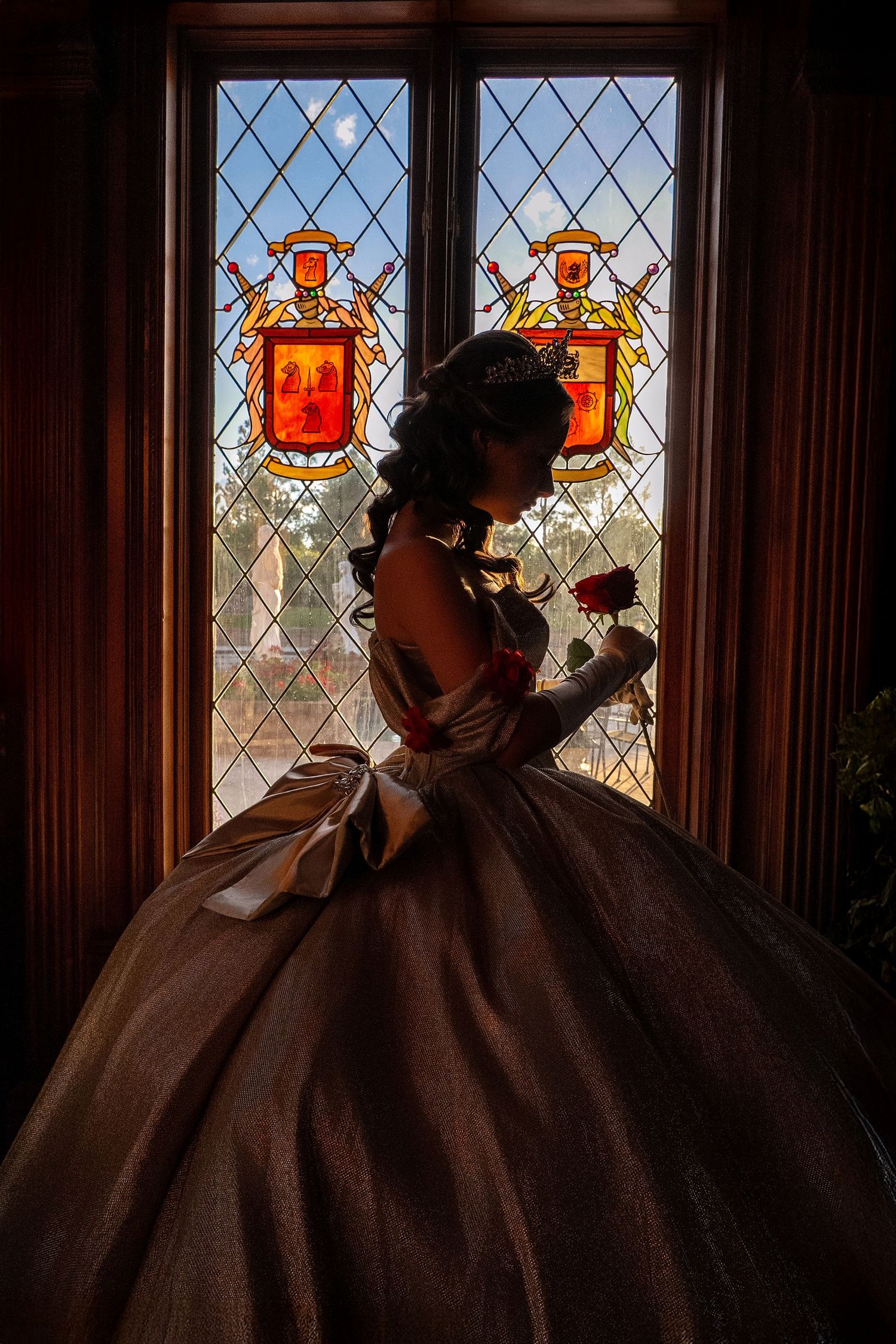 Silhouette of a woman in a ballgown holding a rose before stained glass windows in a castle.