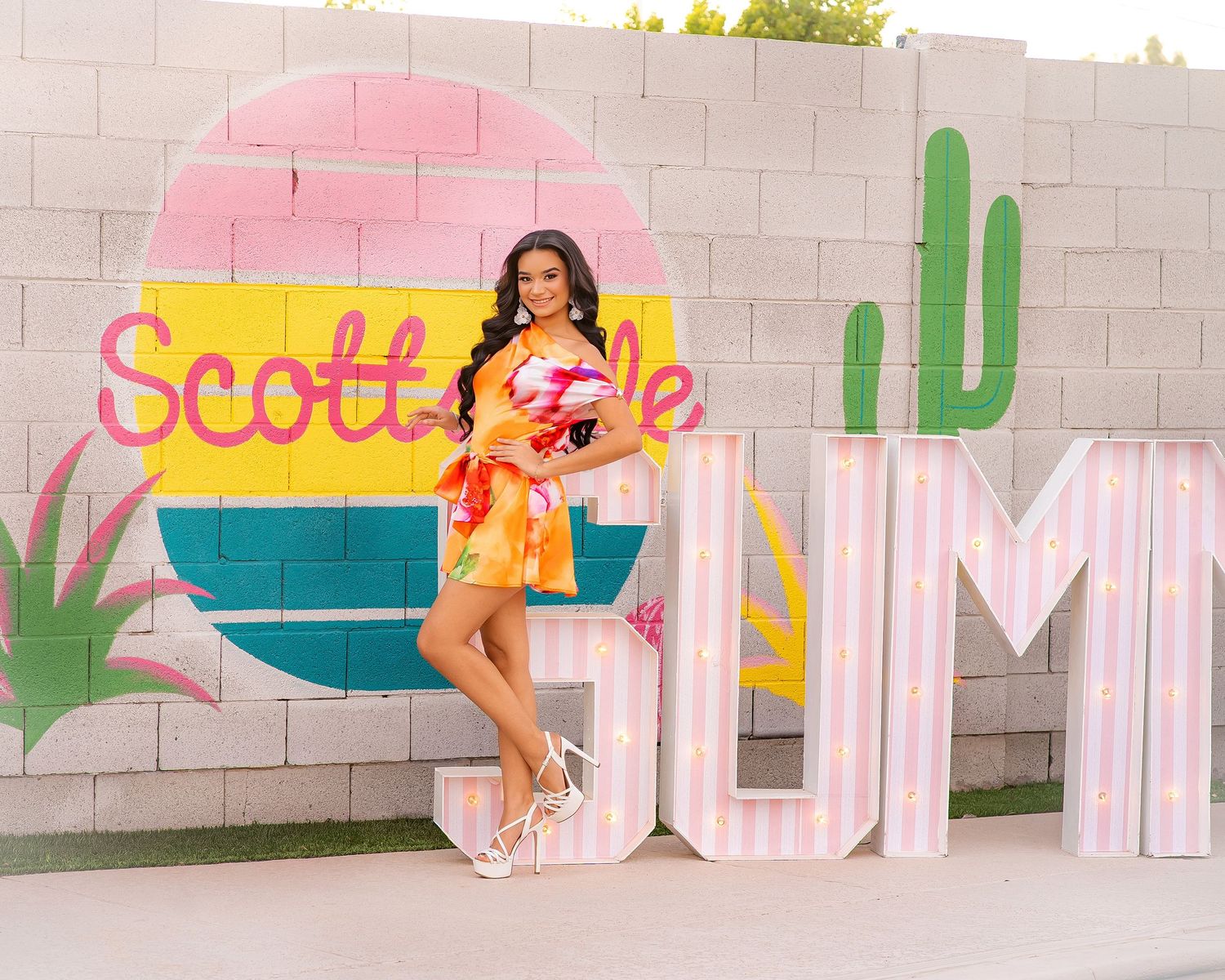 Woman in colorful dress posing by Scottsdale Summer mural with cactus art and large marquee letters outdoors.