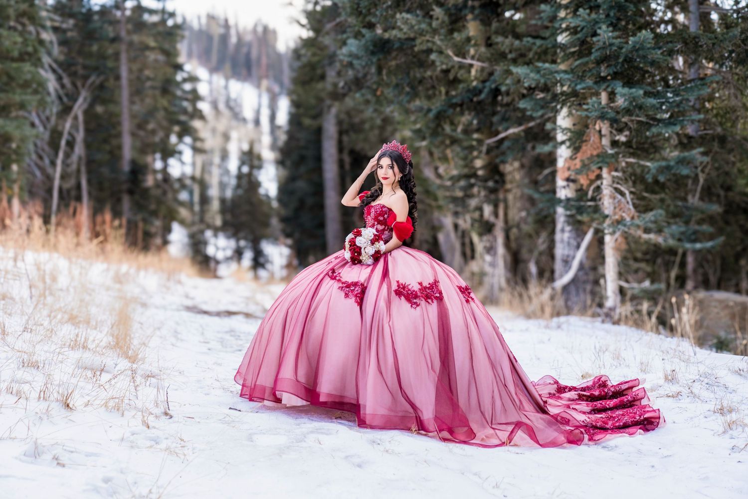 Woman in a red ballgown wedding dress posing in a snowy winter forest landscape.
