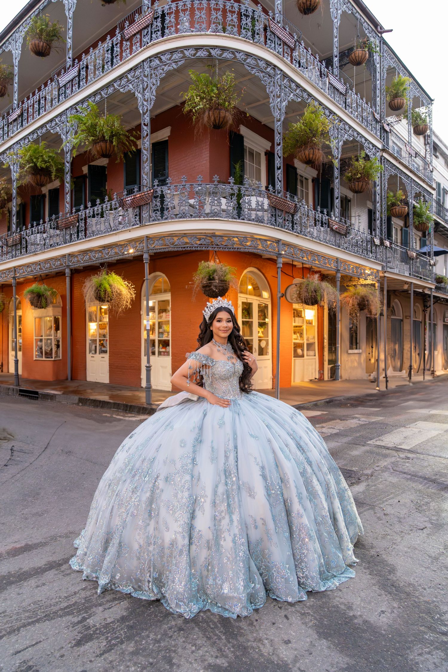 Young woman in a light blue quinceañera ball gown poses in New Orleans French Quarter with ornate iron balconies.