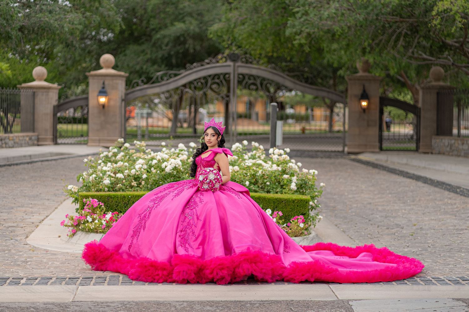 Young woman in a stunning hot pink quinceañera ball gown with feather trim poses by a floral garden gate.