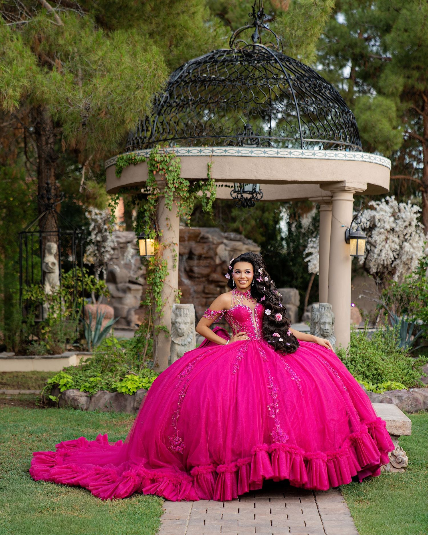 Young woman in a vibrant hot pink quinceañera ball gown posing in front of an elegant garden gazebo.