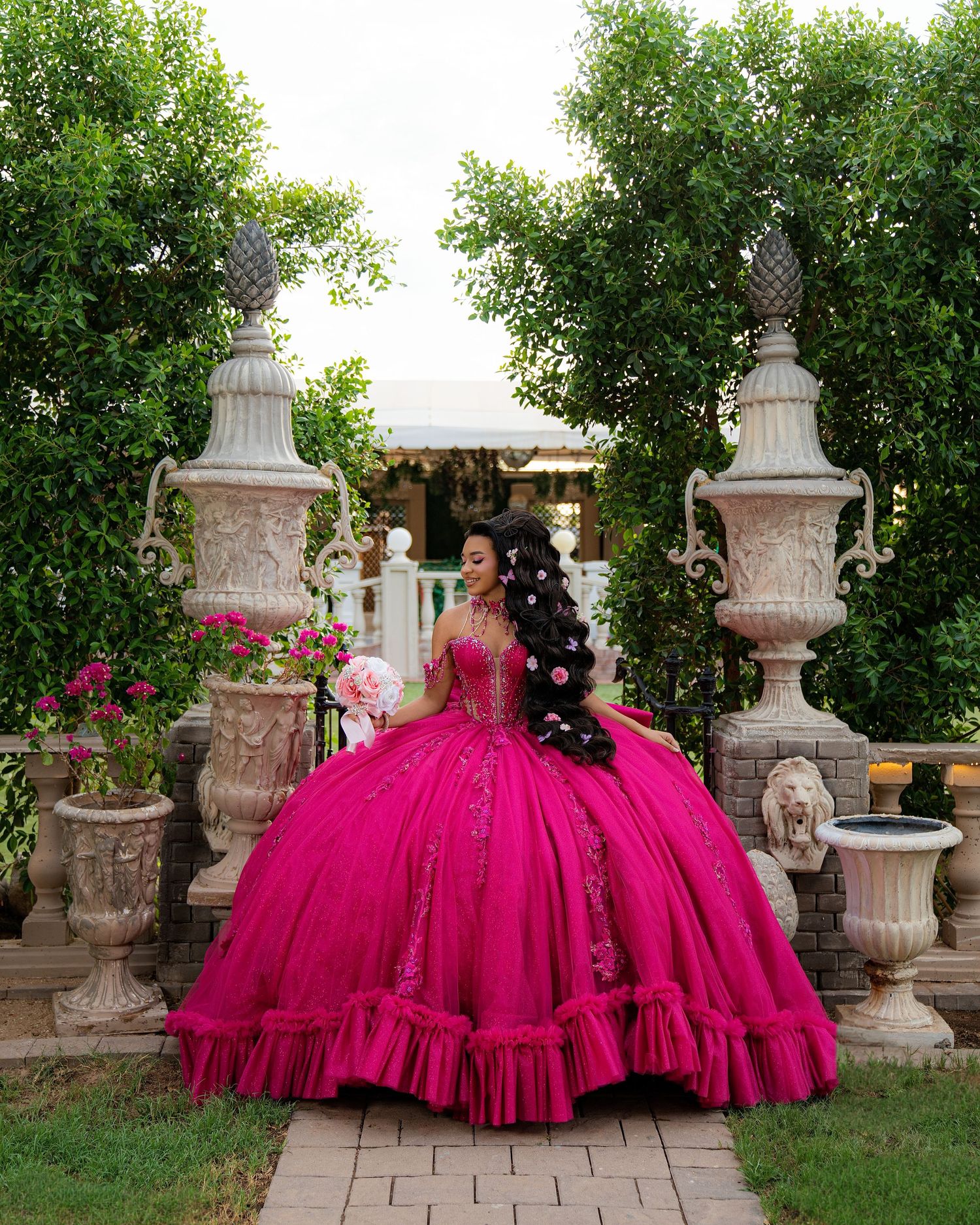 Young woman in a stunning fuchsia quinceañera ball gown with floral details poses in an elegant garden setting.