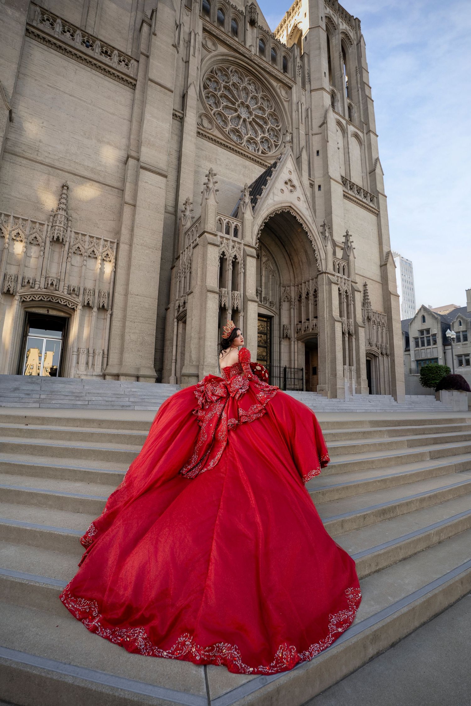 Woman in red ballgown quinceañera dress poses on cathedral steps in an elegant architectural setting.