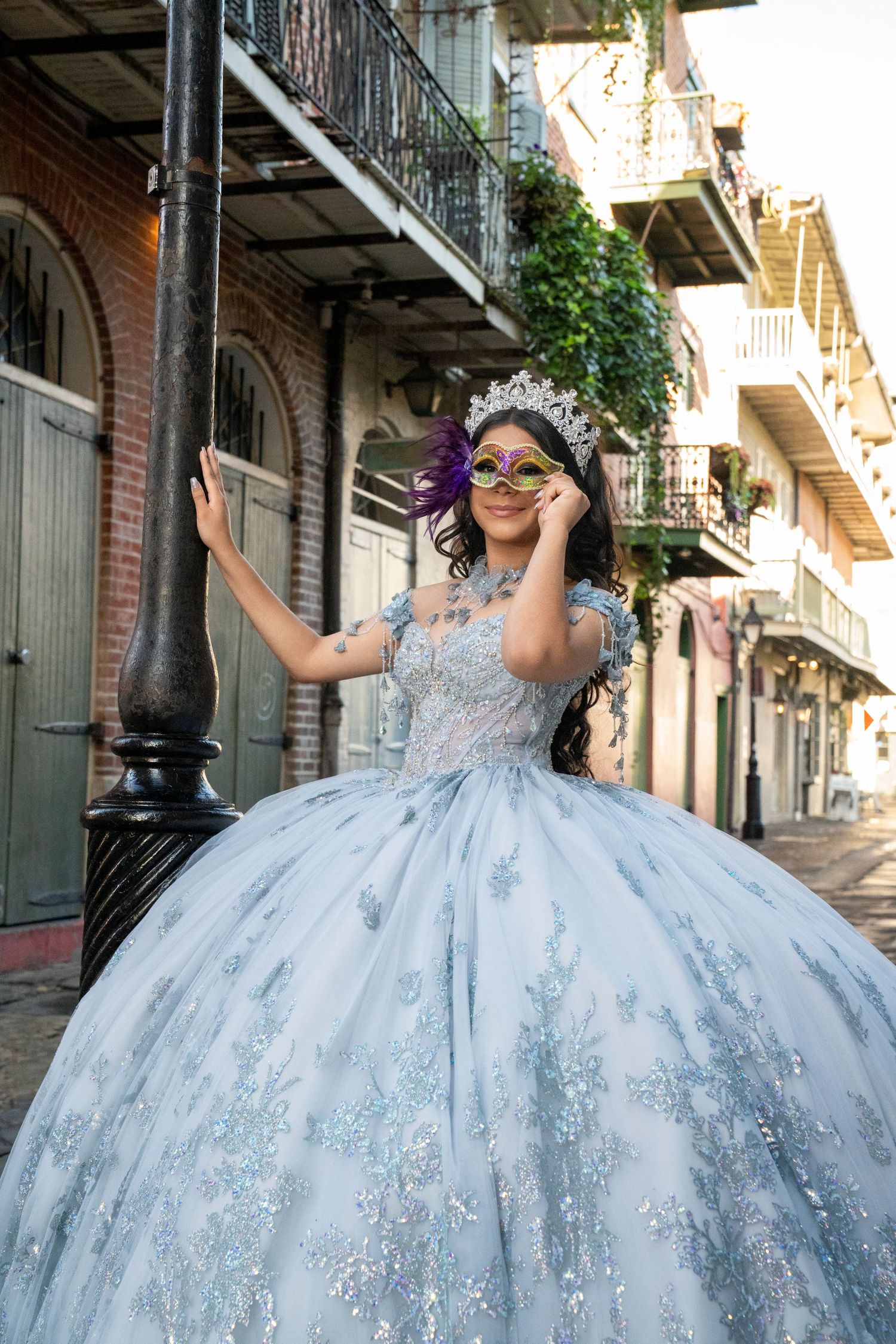 Young woman in a light blue quinceañera ball gown and masquerade mask posing on a New Orleans French Quarter street.