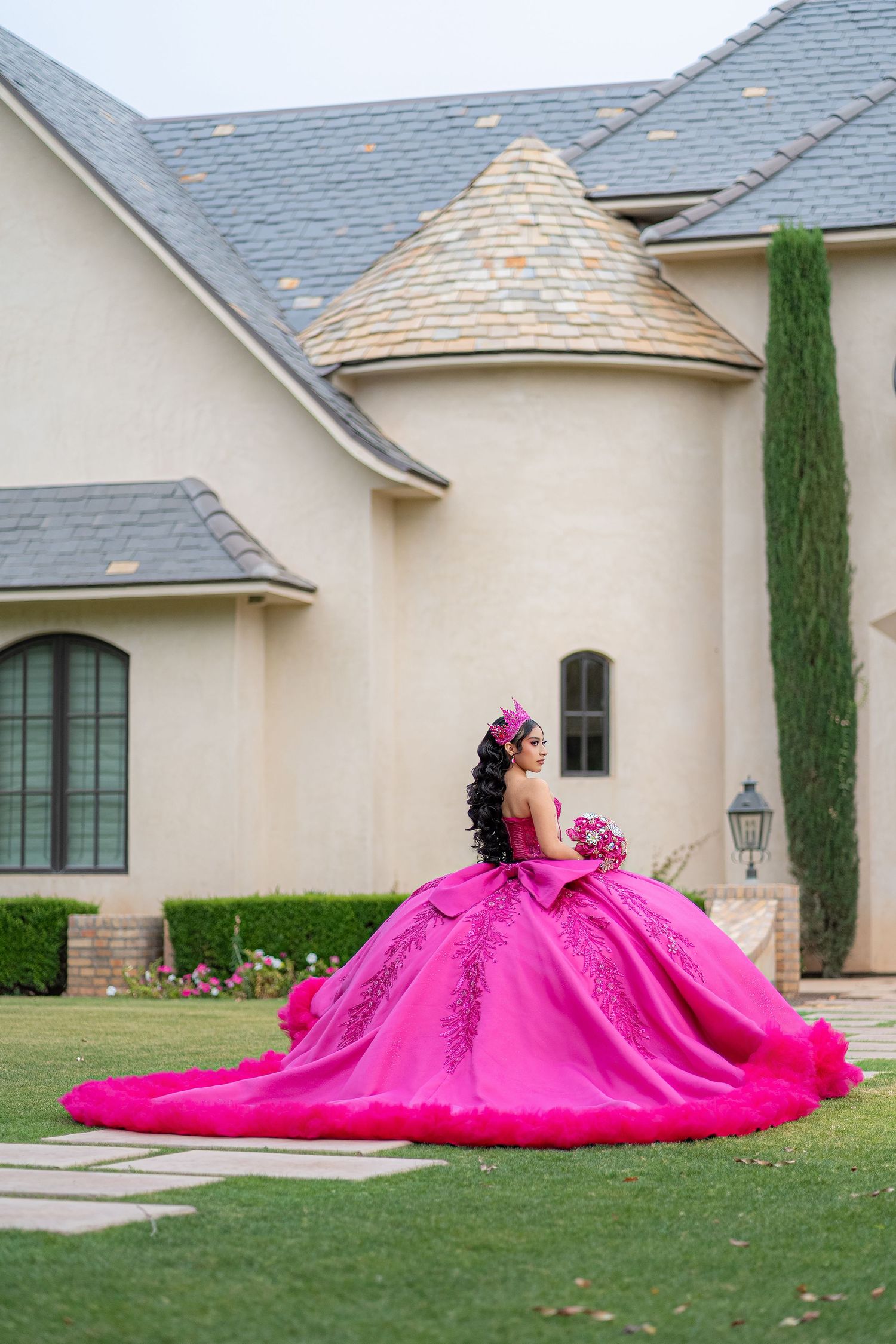 Young woman in a stunning hot pink quinceañera ball gown with floral details poses gracefully outside an elegant estate.