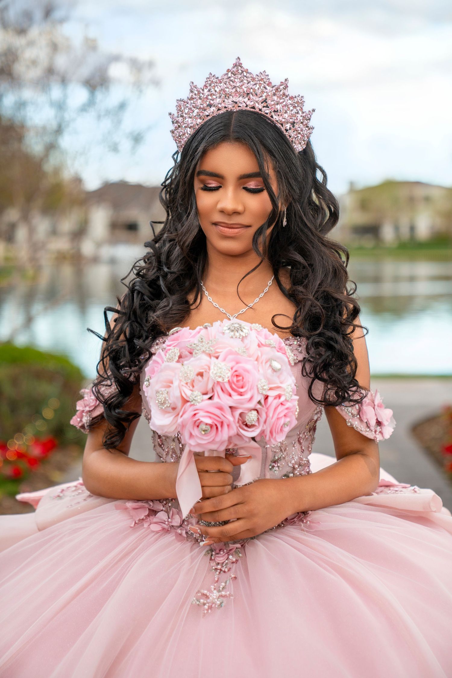 Young woman in pink quinceañera ball gown with floral crown holds pink rose bouquet outdoors.