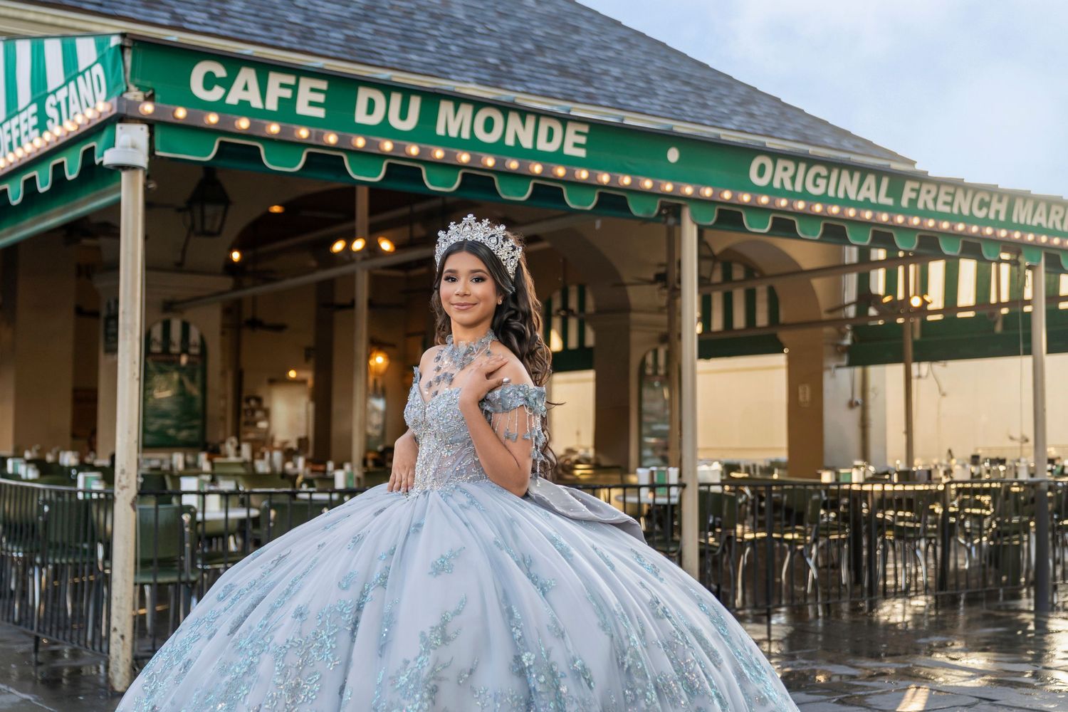 Young woman in elegant quinceañera gown poses in front of Cafe Du Monde in New Orleans French Market.