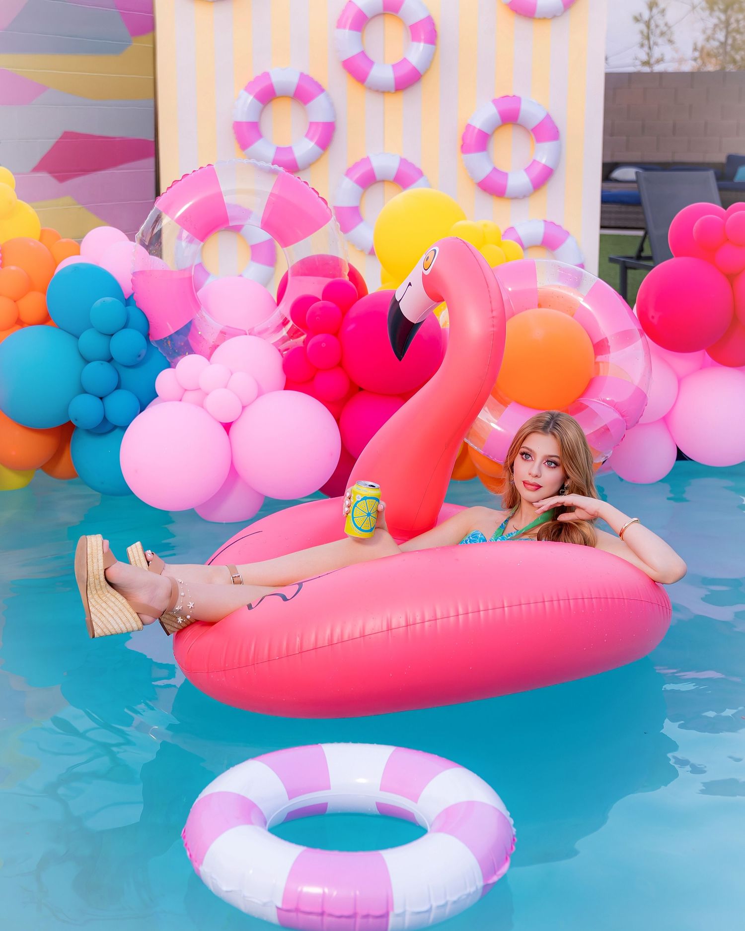 Woman relaxing on pink flamingo pool float surrounded by colorful balloons at a festive pool party.