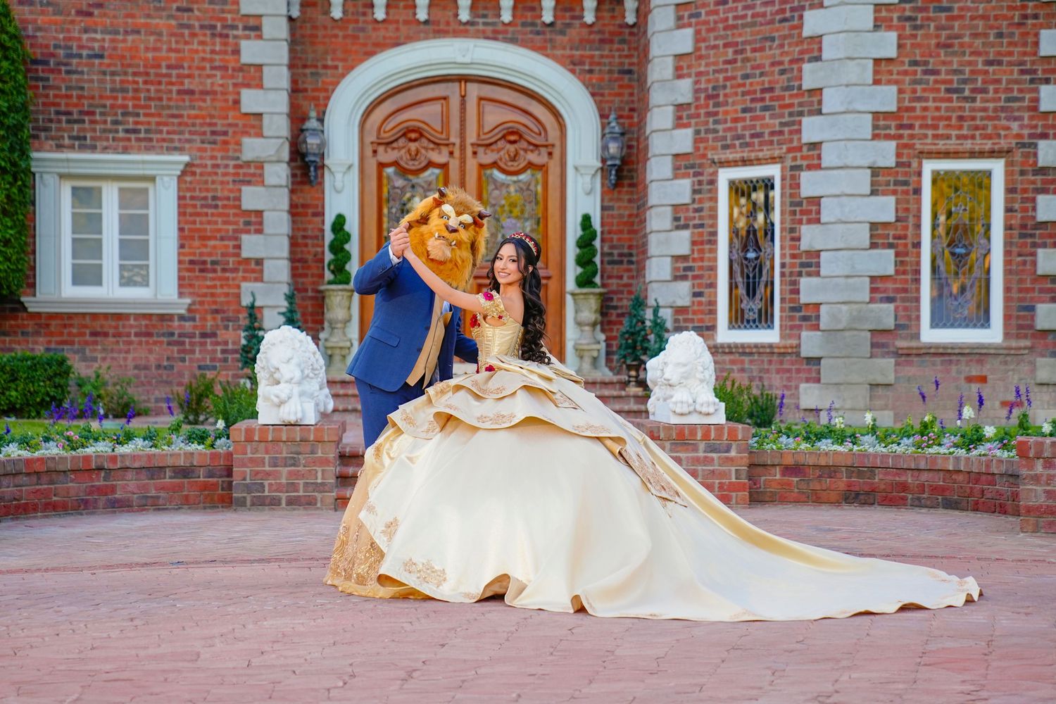 Couple in Beauty and the Beast costumes pose in gold ball gown before a grand brick estate entrance.