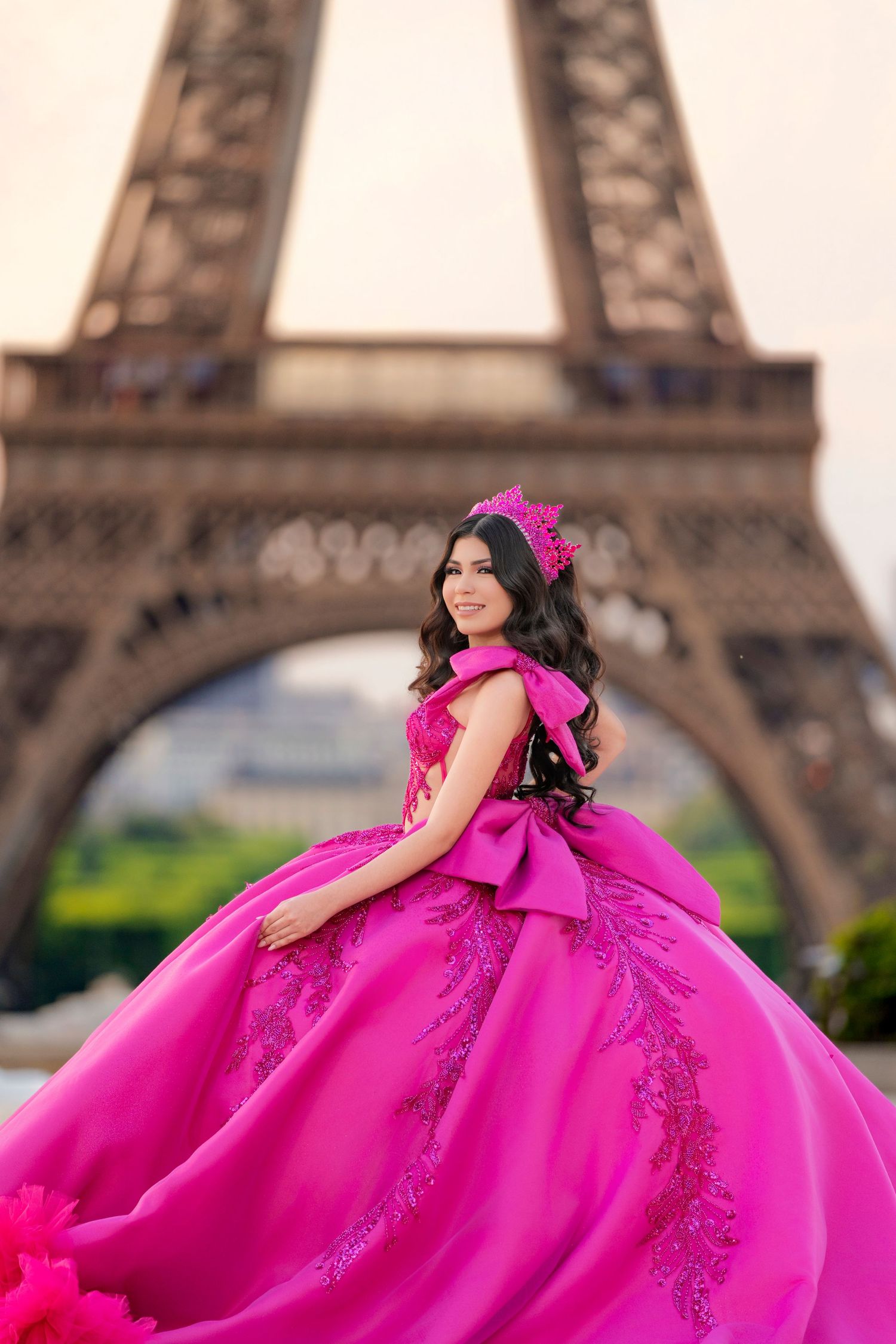 Young woman in pink quinceañera ball gown poses before the Eiffel Tower.