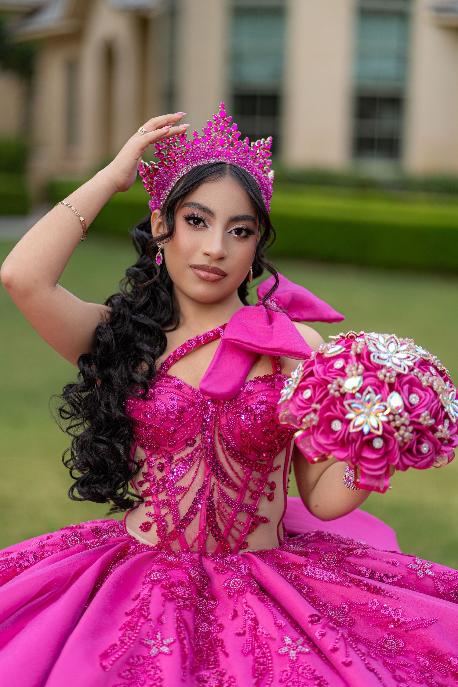 Young Latina in hot pink quinceañera ball gown with crown and floral bouquet poses outdoors.