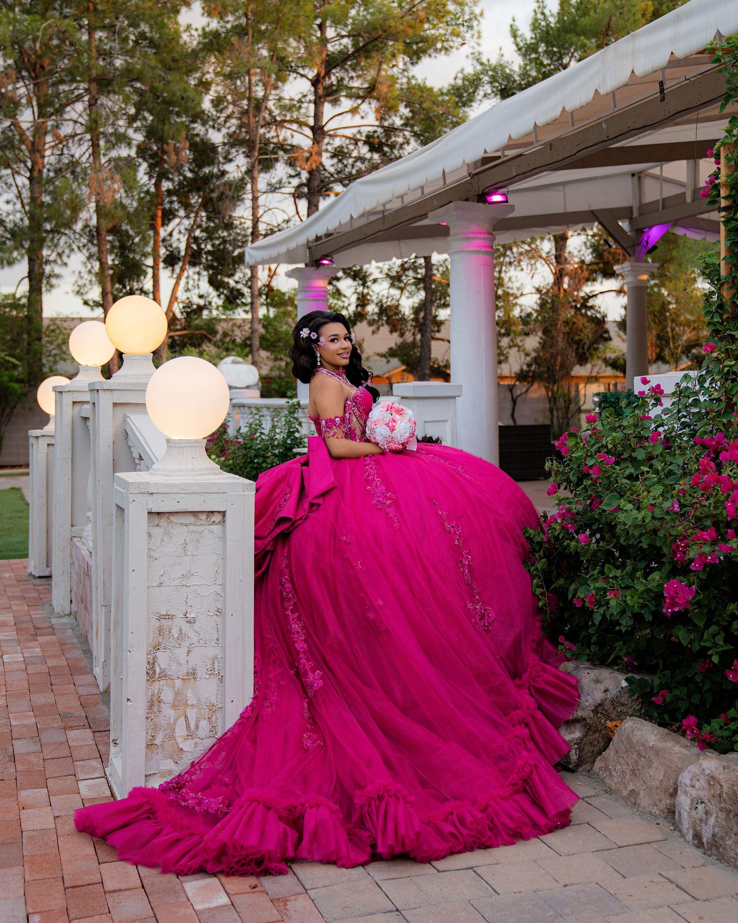 Young woman in a stunning hot pink ball gown poses gracefully at an elegant outdoor venue with white pillars.