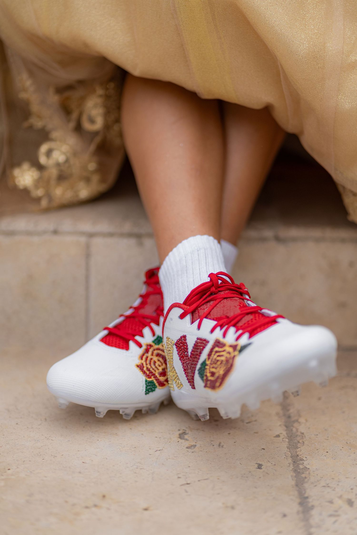 Custom white and red rose-embroidered cleats with gold details worn under a gold quinceañera gown.