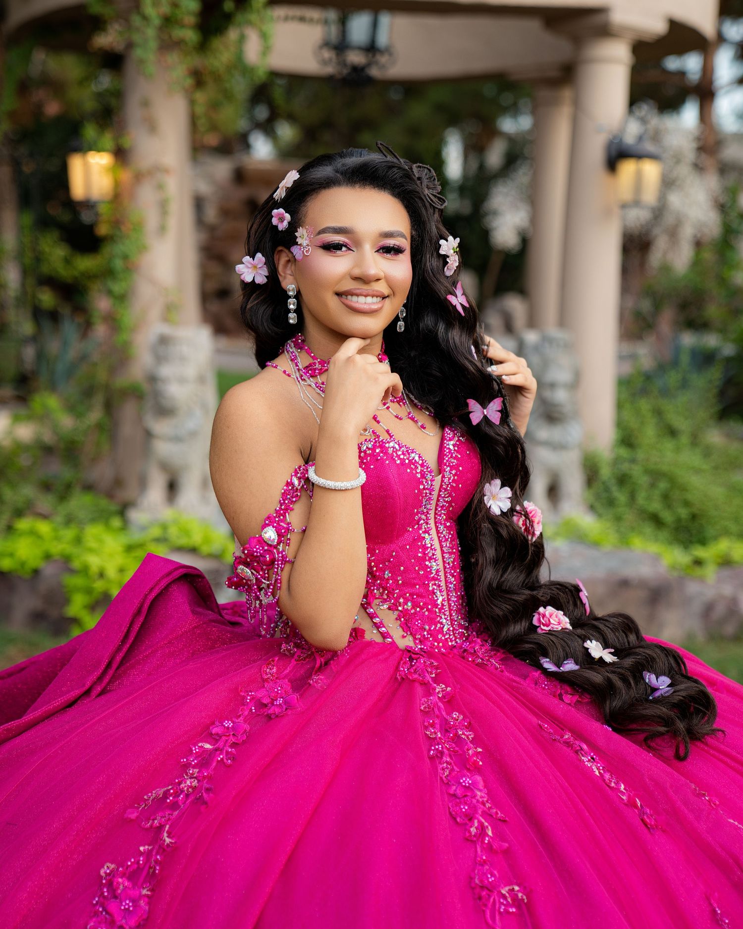 Young woman in a vibrant hot pink quinceañera ball gown with floral accents and butterfly hair accessories.