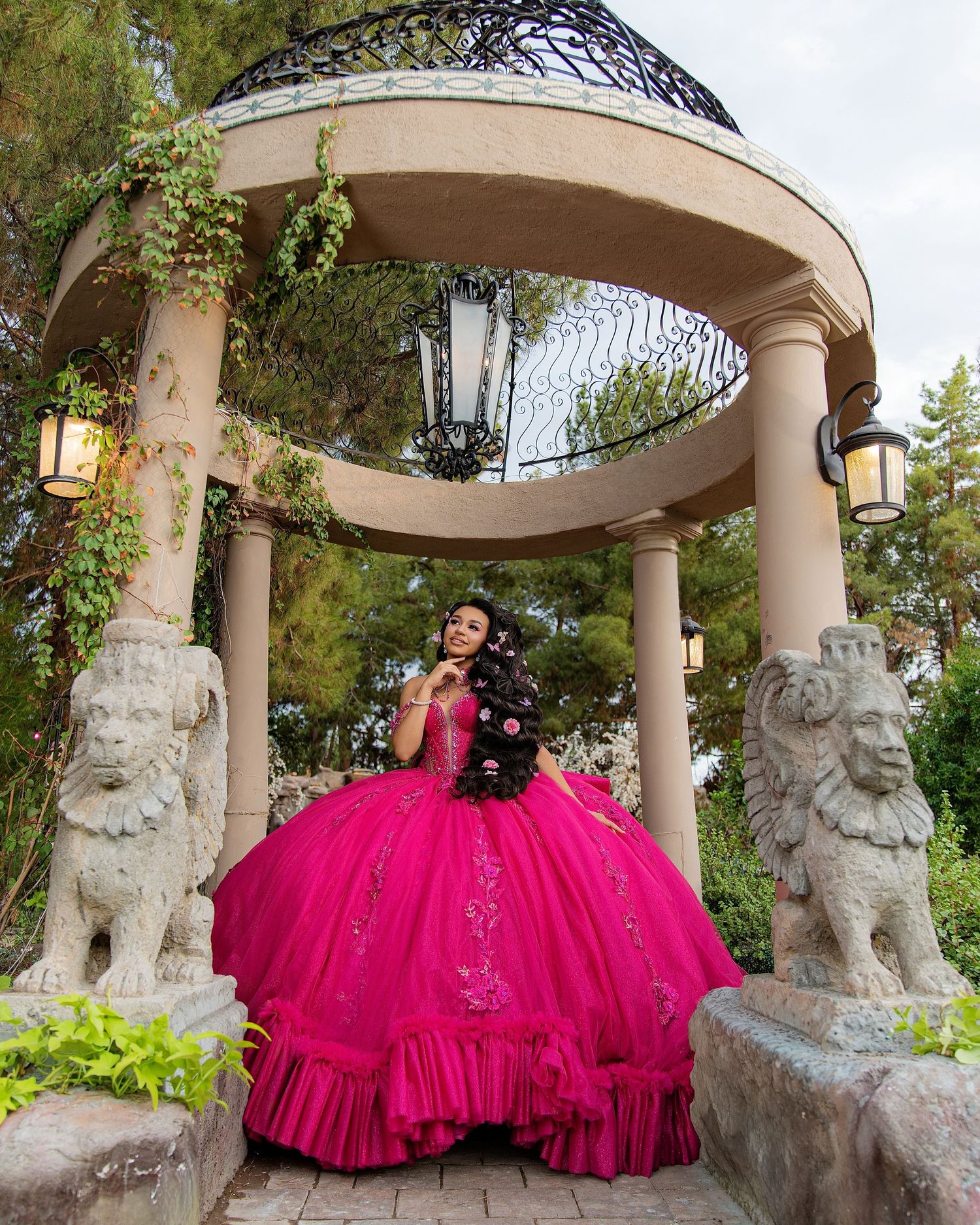 Young woman in a vibrant hot pink quinceañera ball gown posing in an elegant gazebo with lion statues.