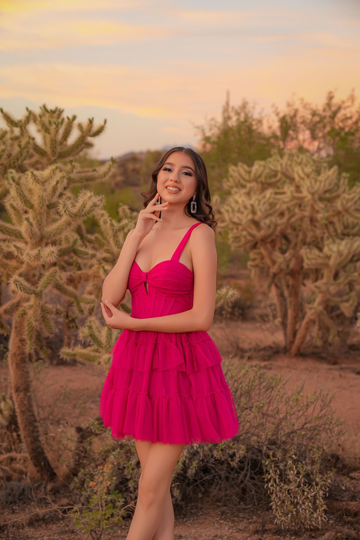 Young woman in pink tulle mini dress posing among desert cacti at golden hour sunset.
