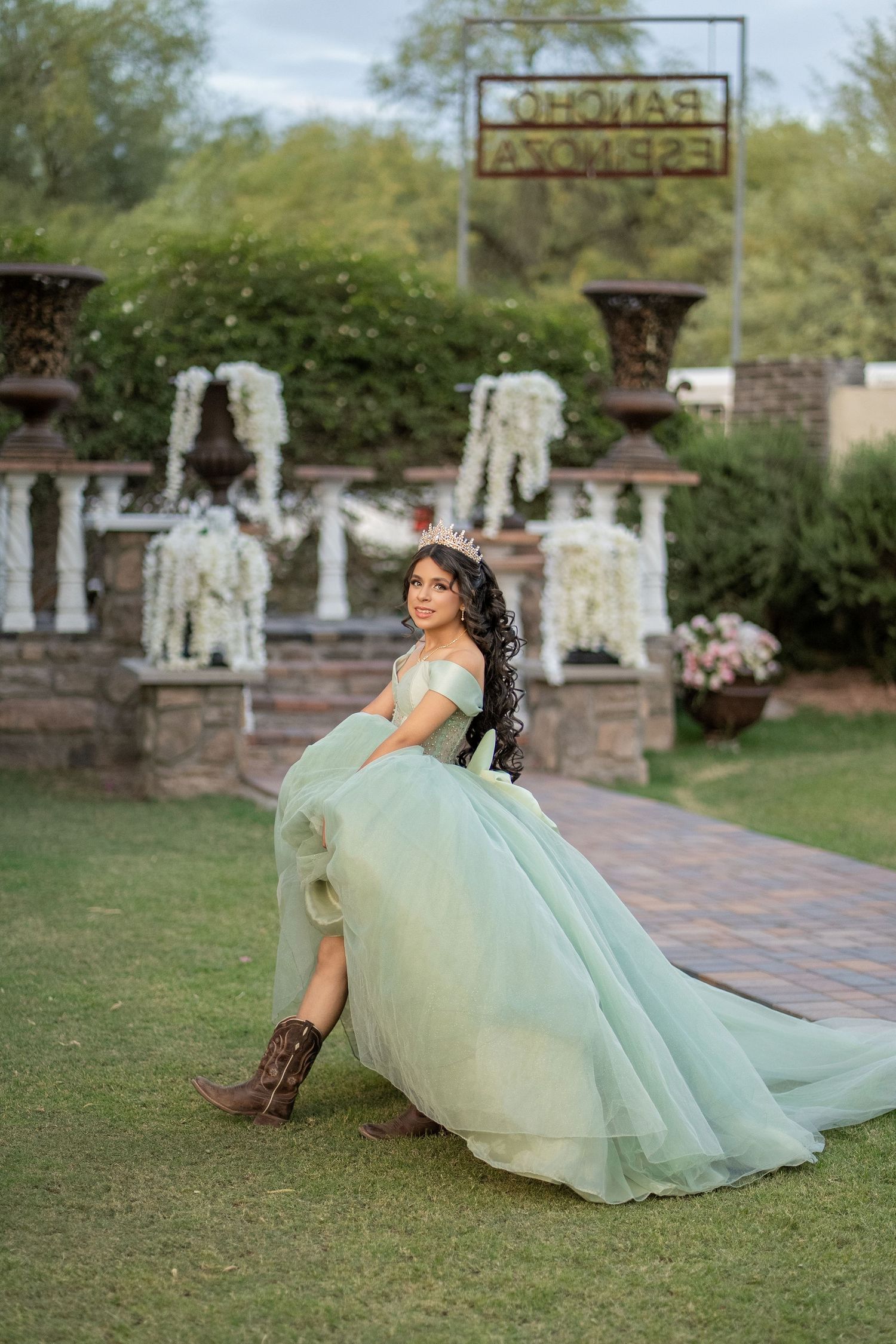 Young woman in mint green quinceañera ball gown with cowboy boots poses at Rancho Espinoza venue.